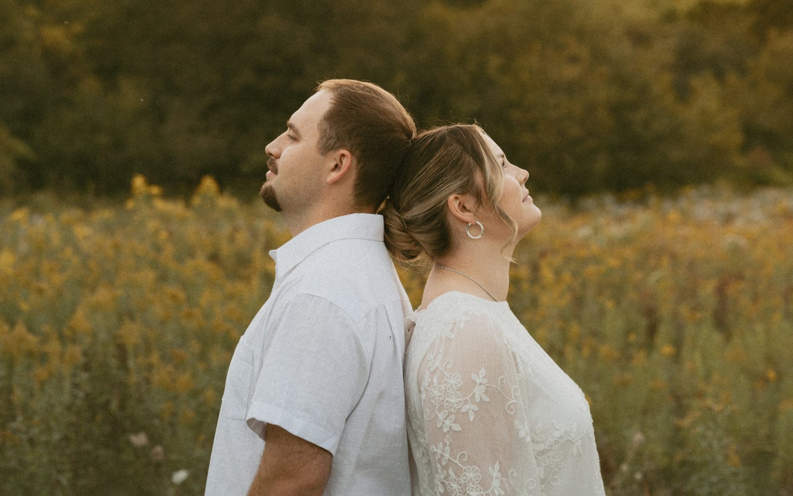 A couple standing back to back in a field of goldenrod, looking up at the evening sky