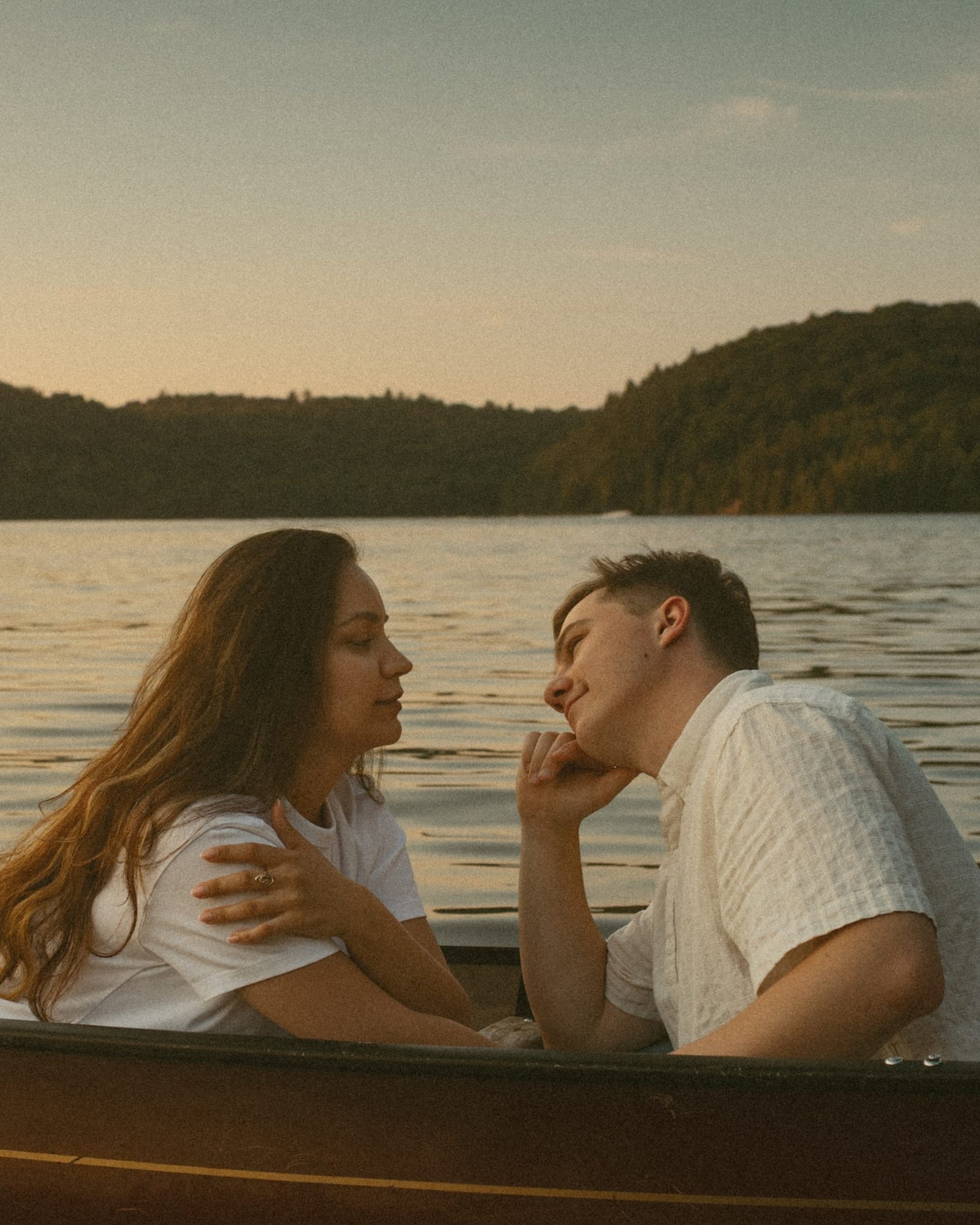 A woman resting against her partner in a red canoe, hills soft behind them