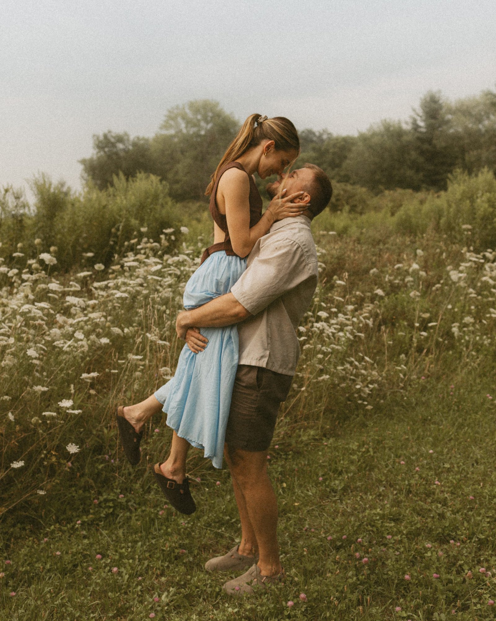 A man lifting his partner into a kiss among Queen Anne's lace, her pale blue skirt swinging