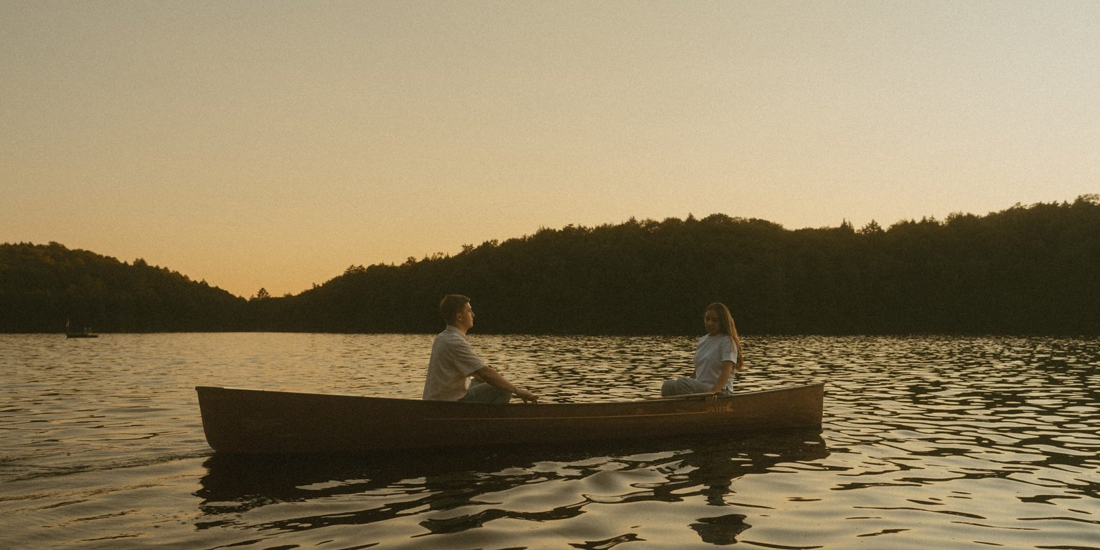 A couple sitting together in a canoe at sunset on a still lake