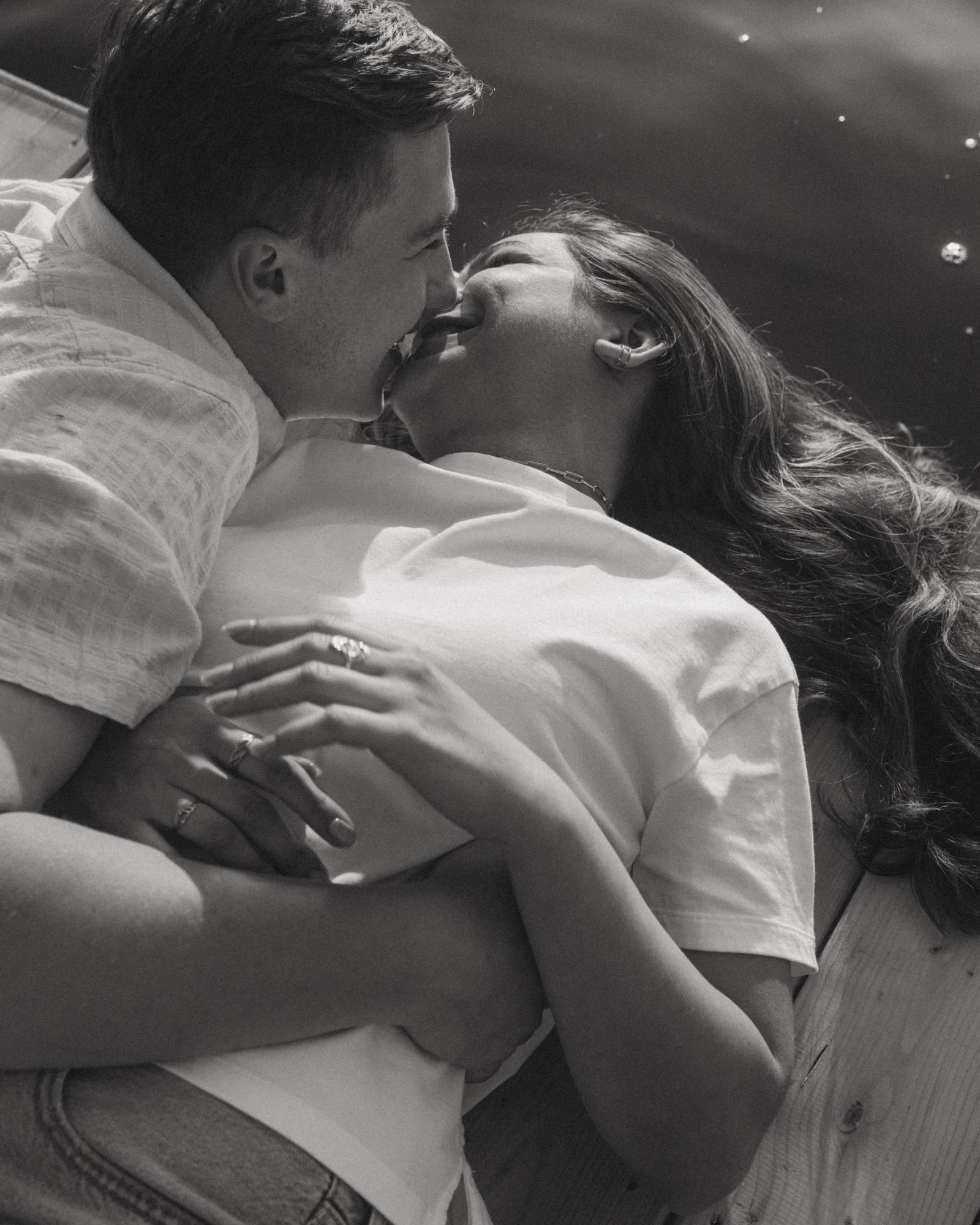 A black and white frame of a couple embracing on a deck in dappled light