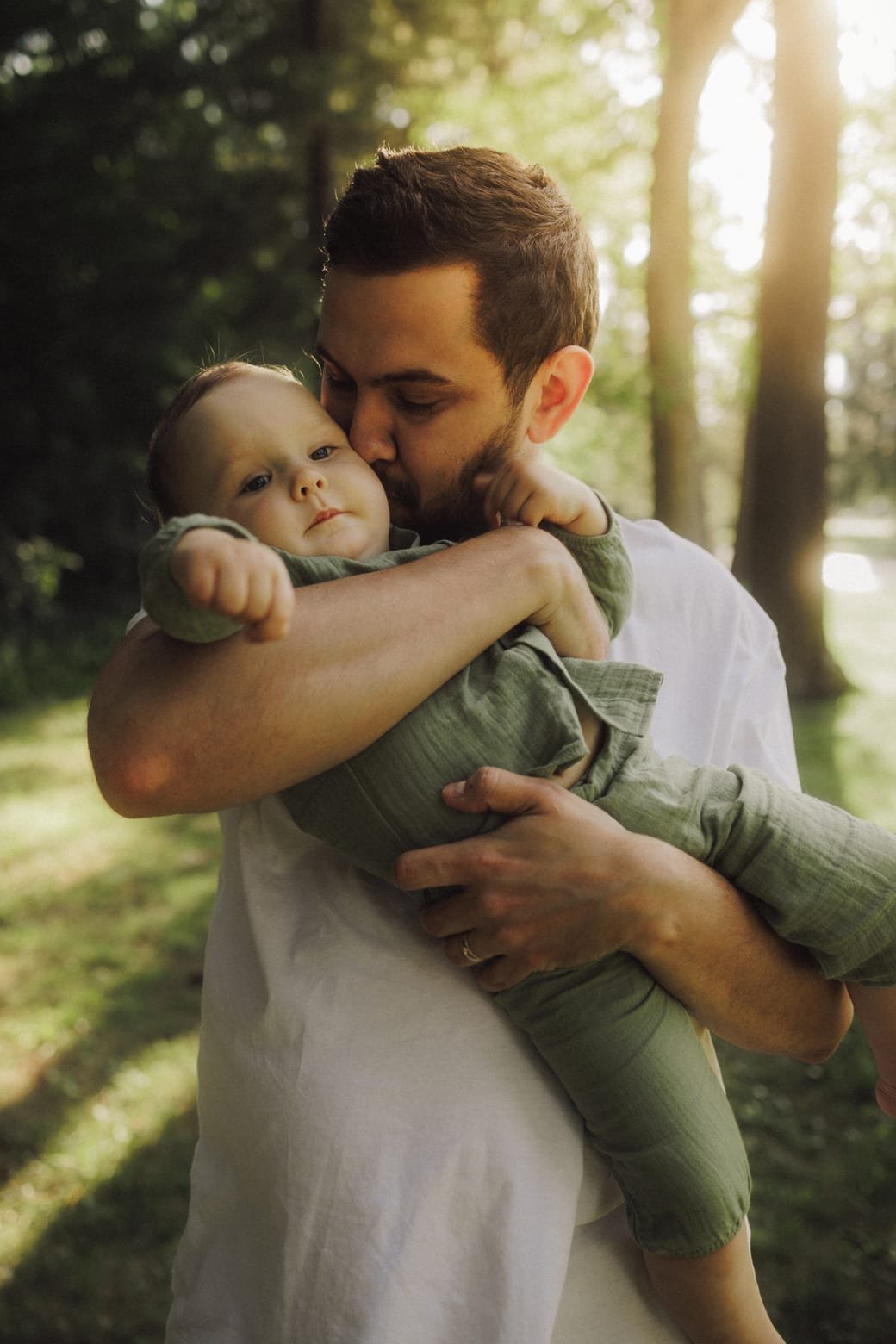 A father carrying his baby son on his shoulder in backlit woodland