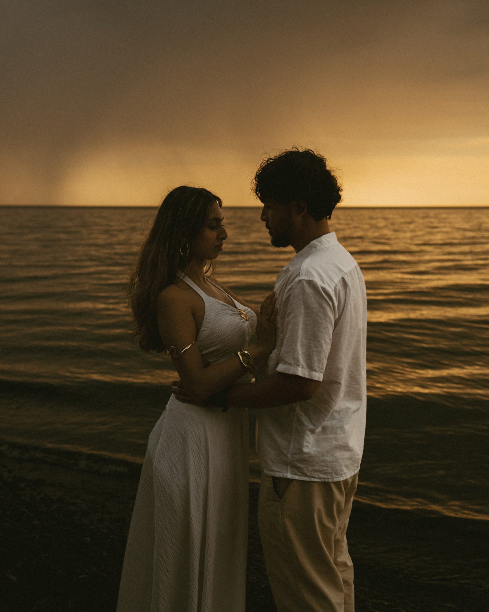 A woman in a white dress facing her partner on the shore of a dark lake