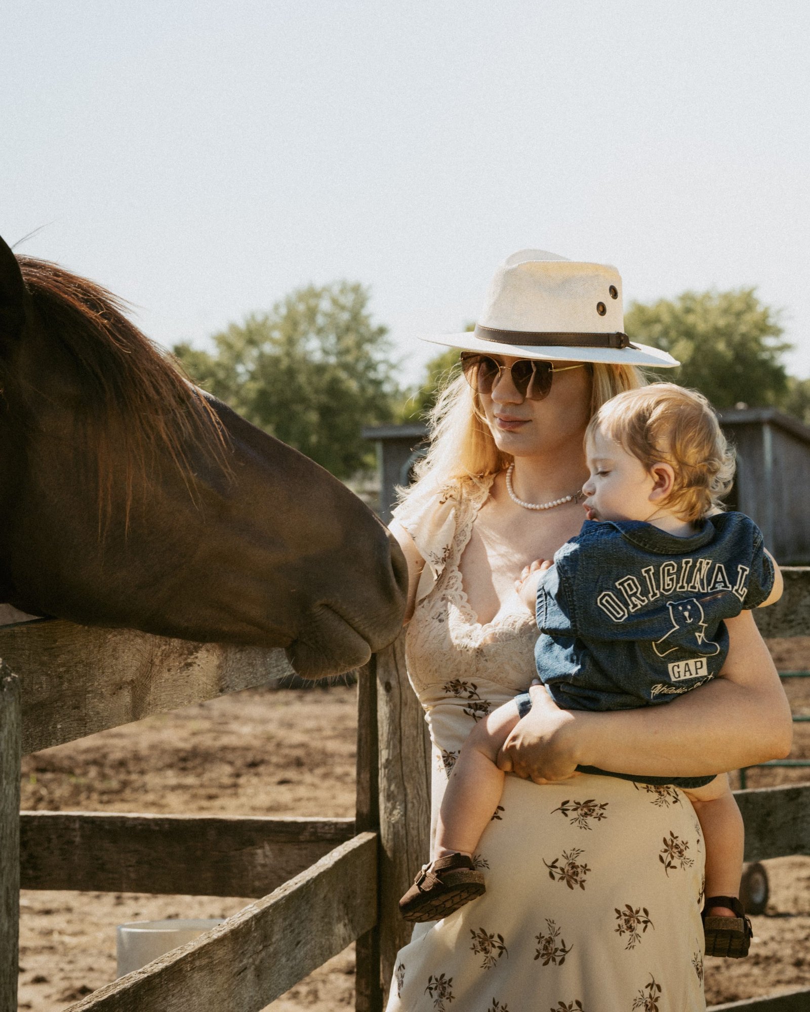 A mother tilting her head down to her son's face while a horse looks on over the fence