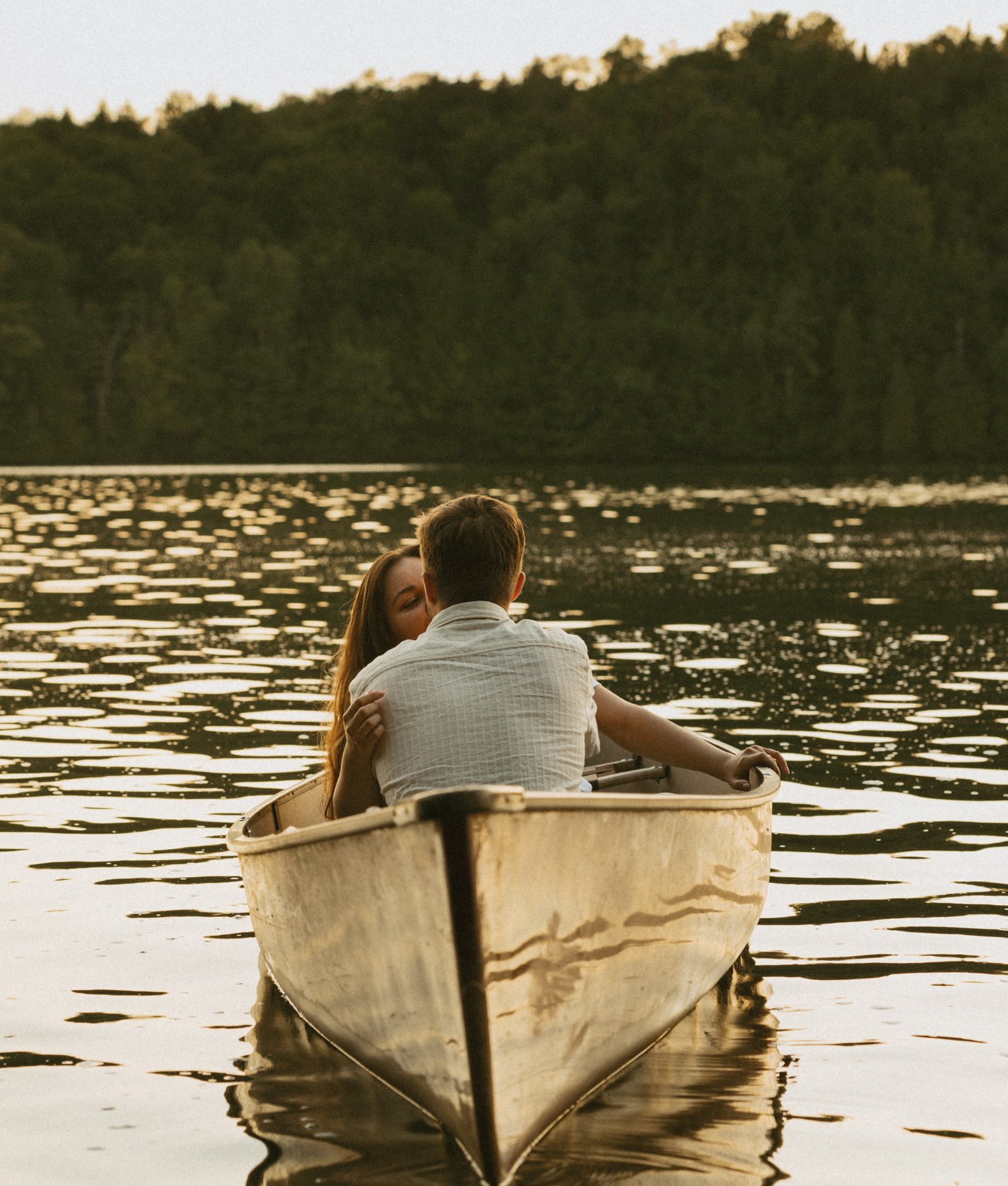 A couple sitting together in a red canoe on calm open water at the end of the day