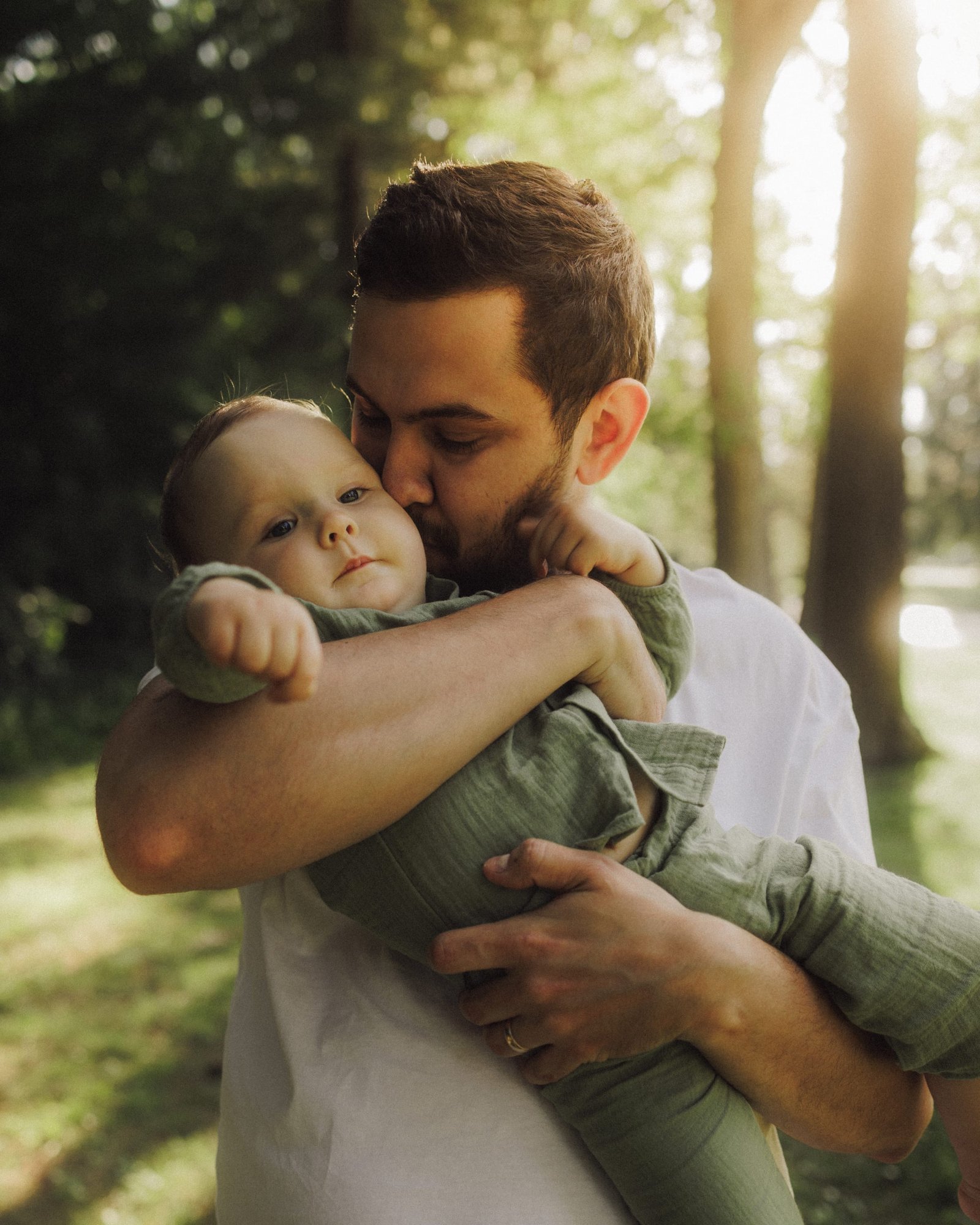 A father carrying his baby son on his shoulder in backlit woodland