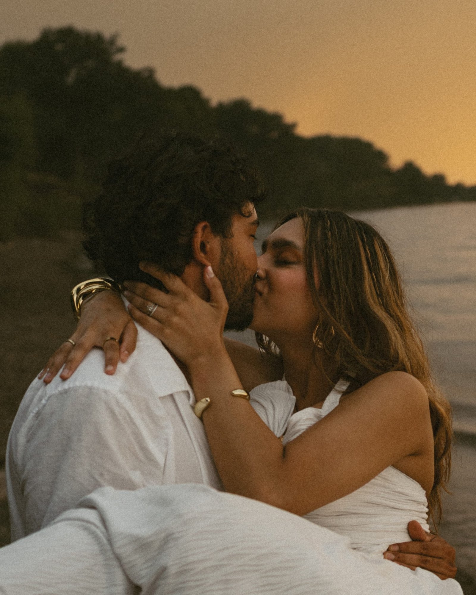 A couple sitting on the shore, her hand on his face and a ring on her finger