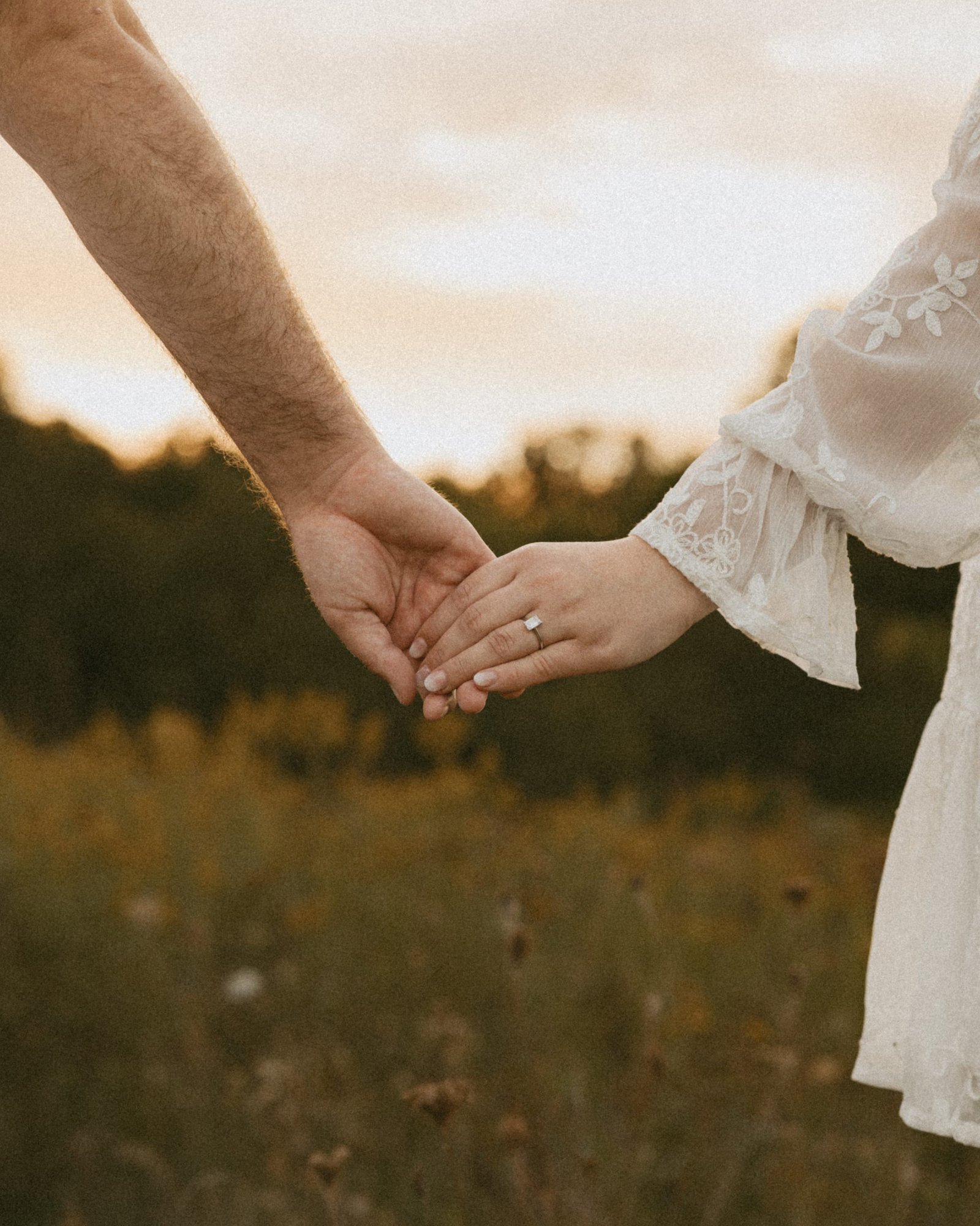 A couple reaching for each other's hands across a golden meadow at sunset