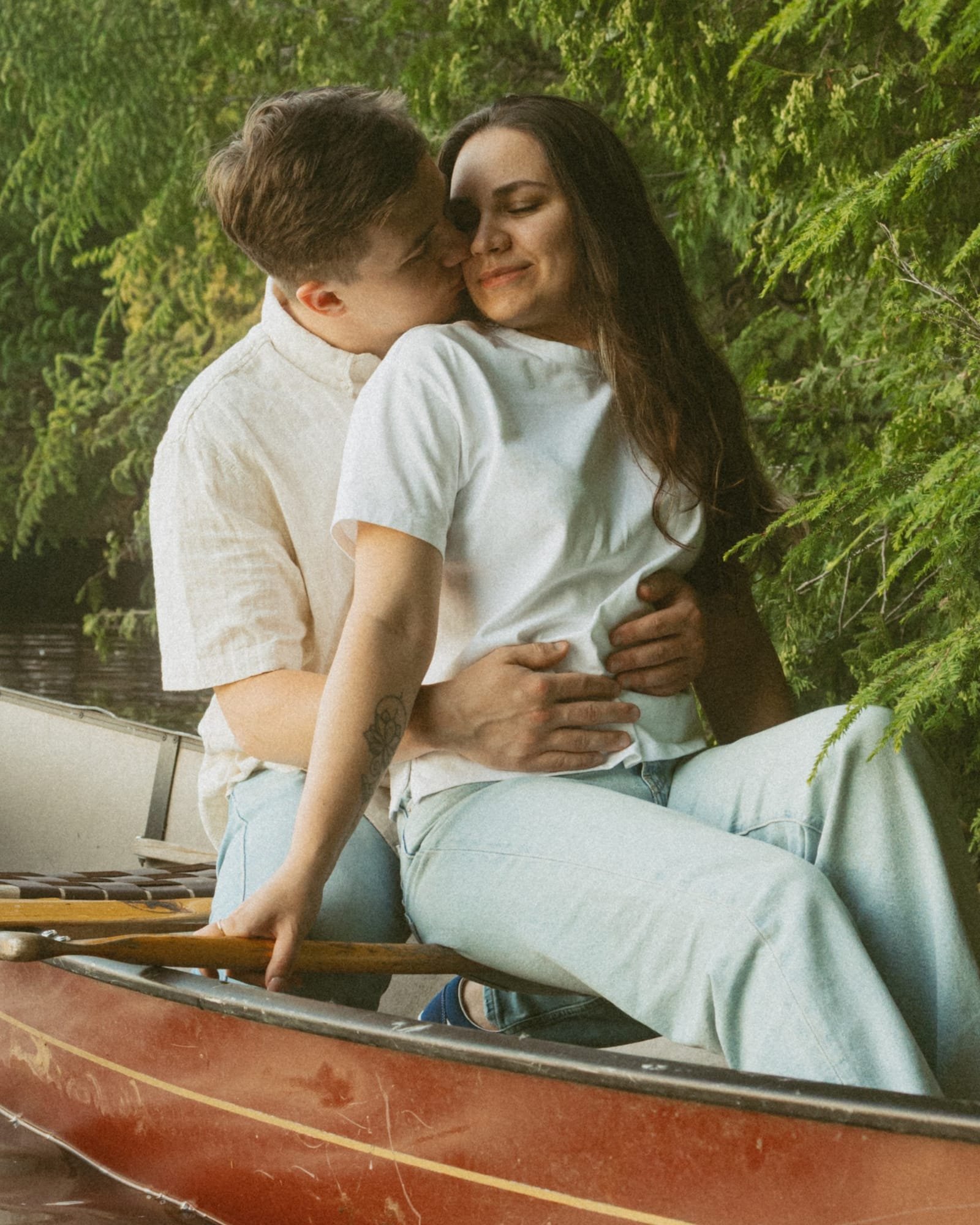 A couple sitting in a canoe at the shoreline, turning to look back at the camera
