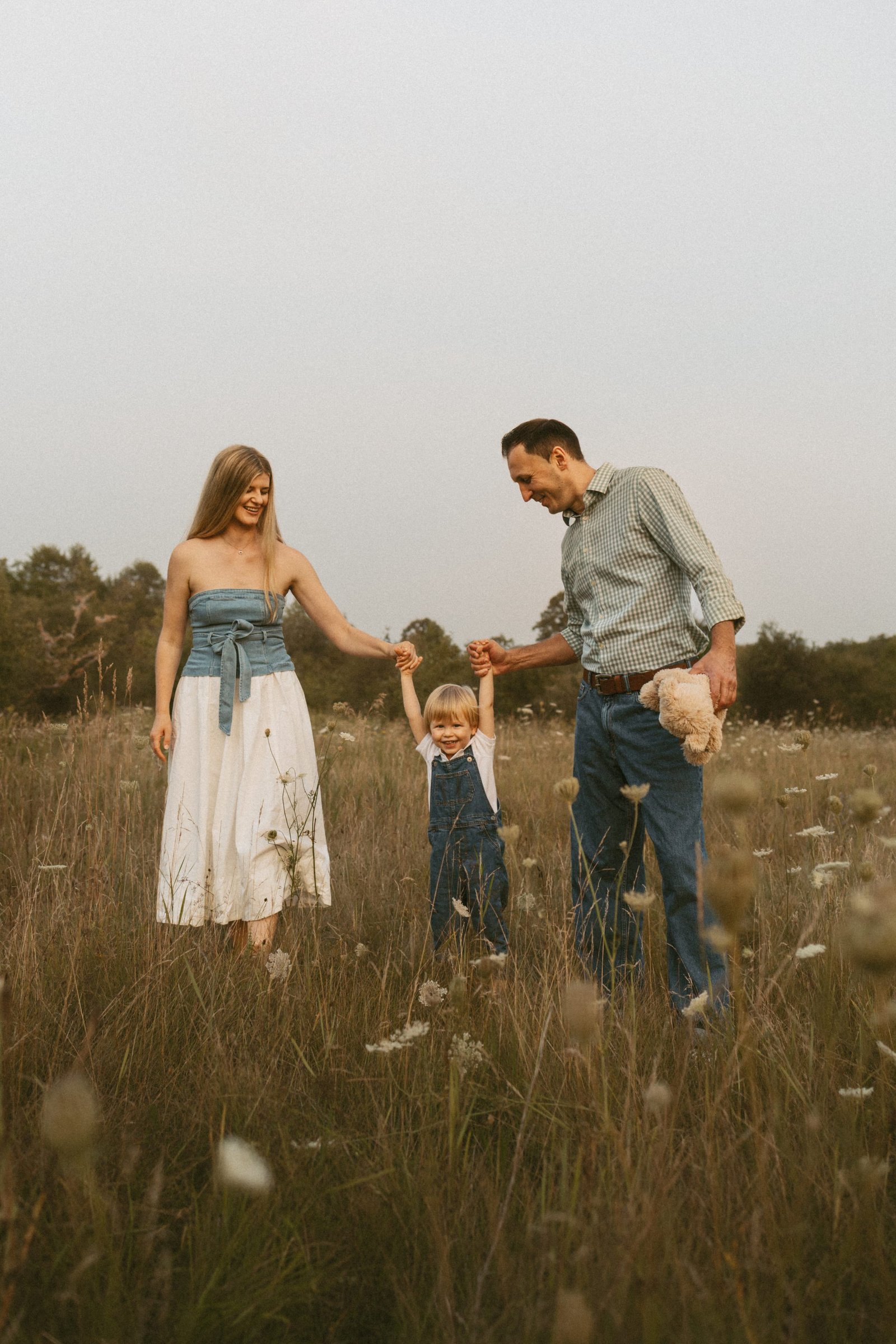 A mother and father swinging their small son between them by the hands in a wide open meadow