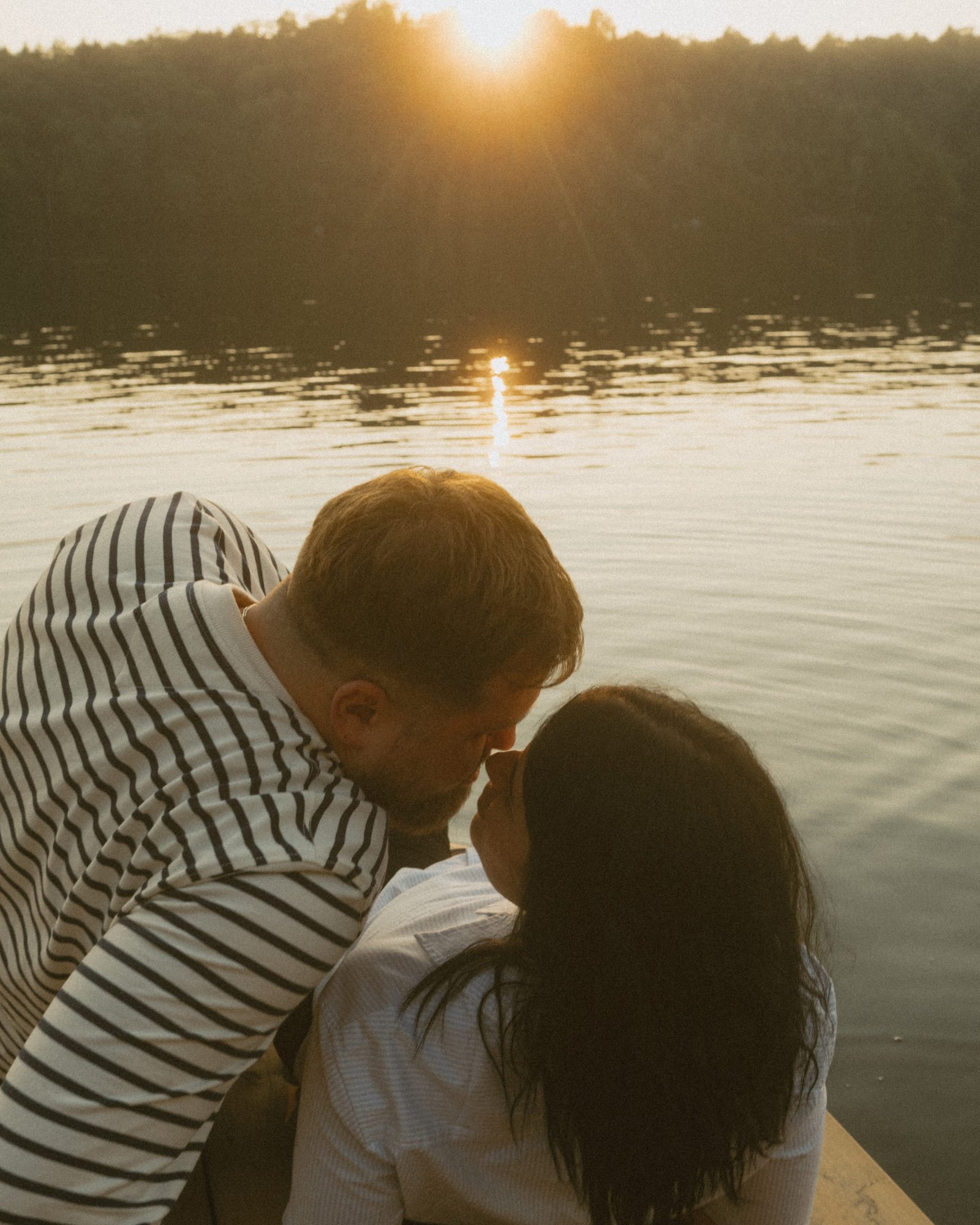 A black and white frame of a couple kissing under backlit trees