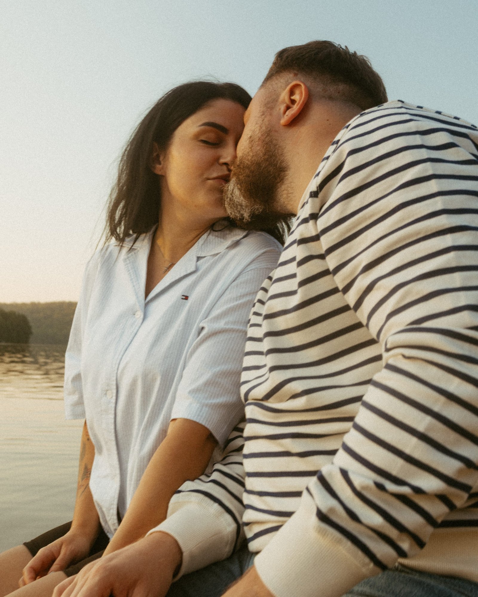 A man leaning down to kiss his partner where she lies on the warm dock boards