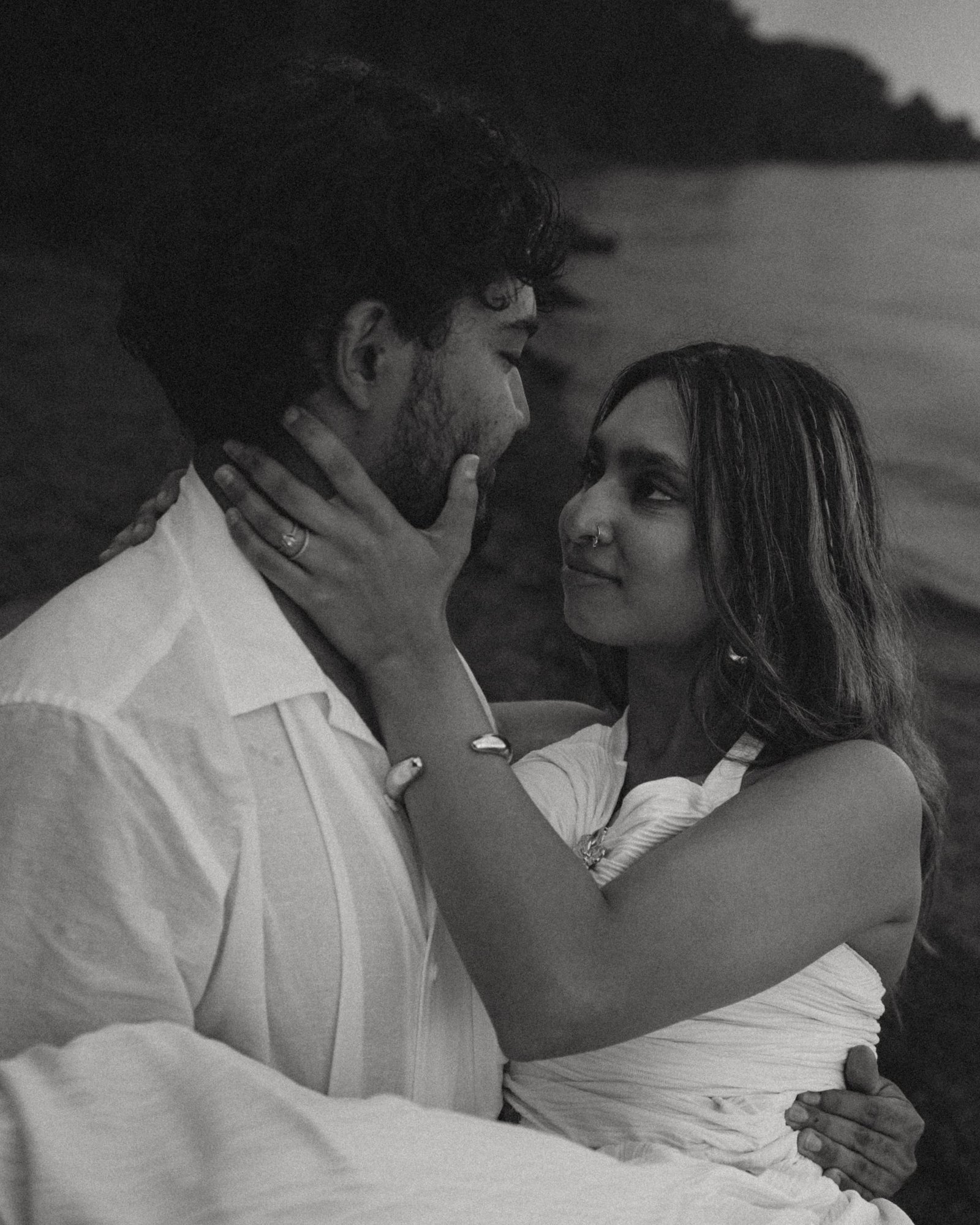 A black and white frame of a couple lying together on the stones by the lake