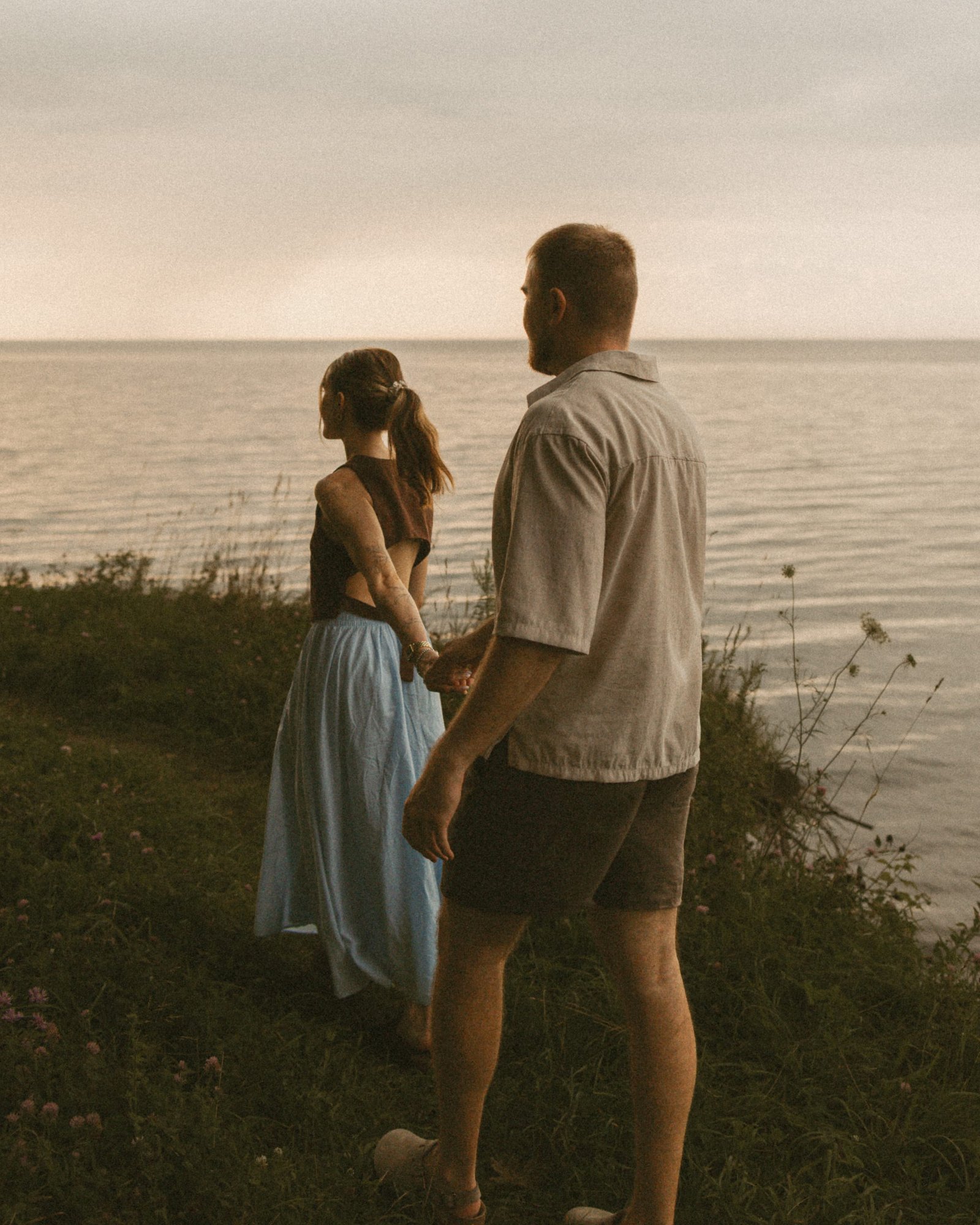 A couple seen from behind standing on the edge of a bluff, looking out over Lake Ontario
