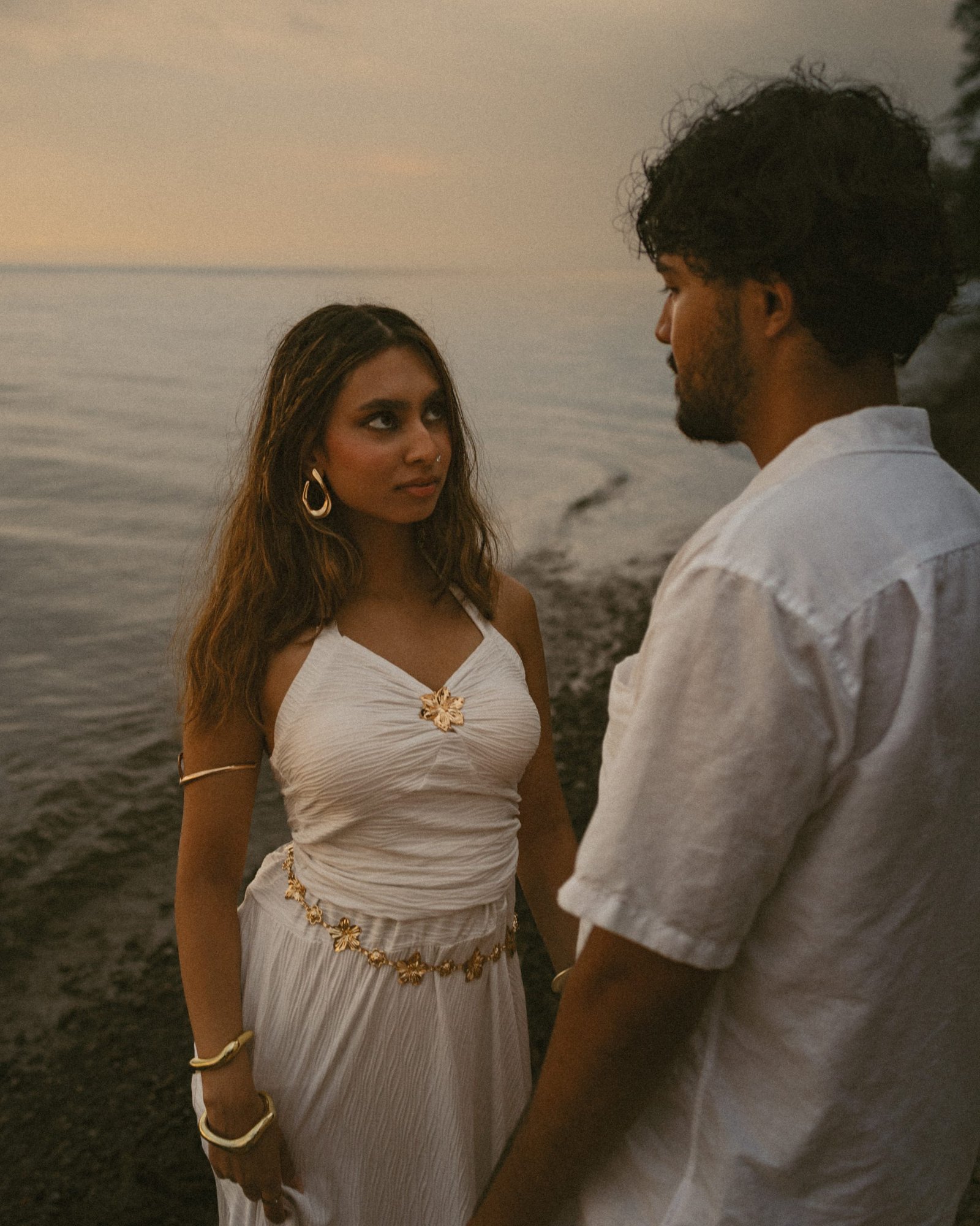A woman looking past the camera while her partner watches her, lake behind them