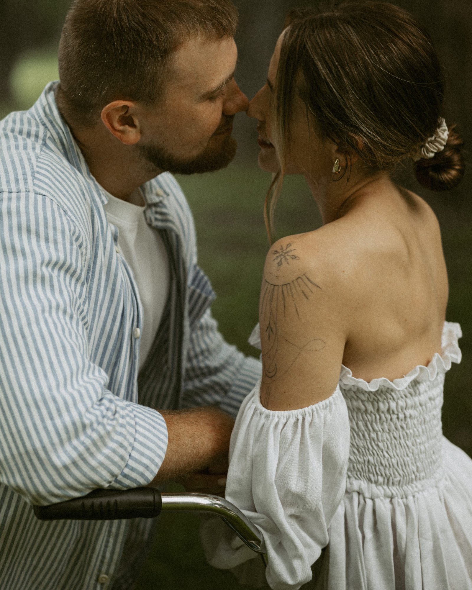 A black and white frame of a couple embracing, her dress bright against the trees