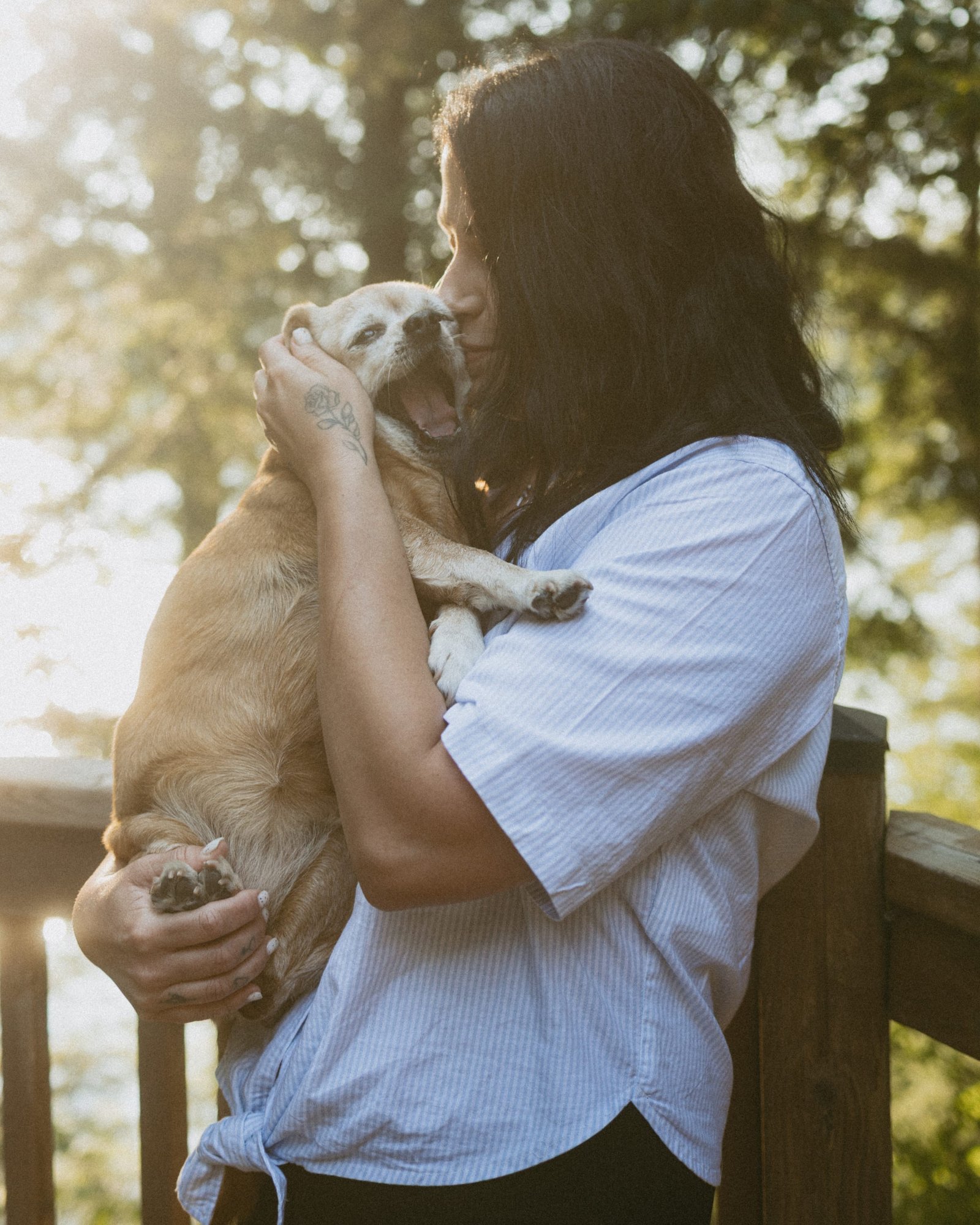 A couple standing close on a wooden deck with sun flaring through the branches behind them