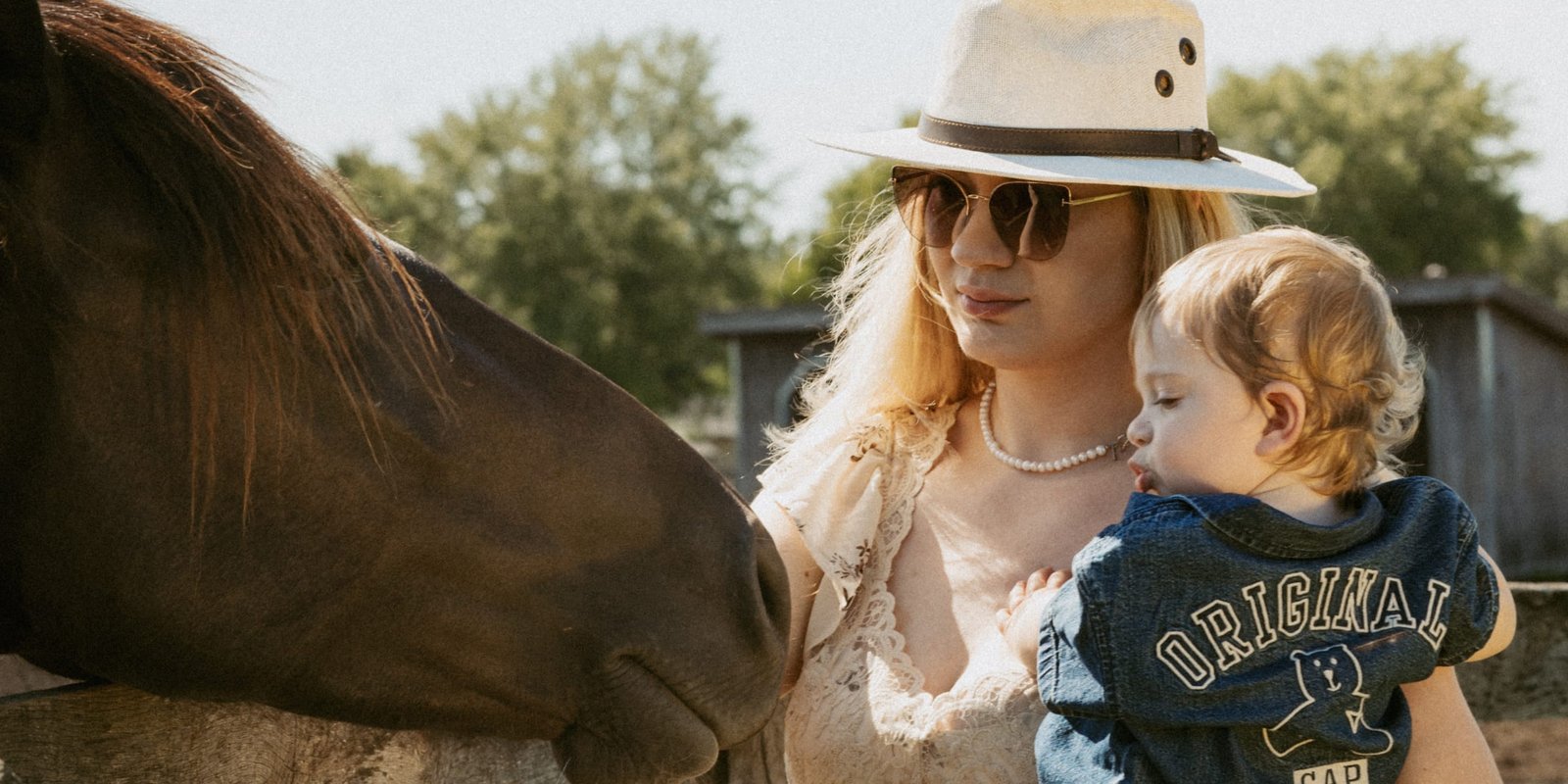 A mother tilting her head down to her son's face while a horse looks on over the fence