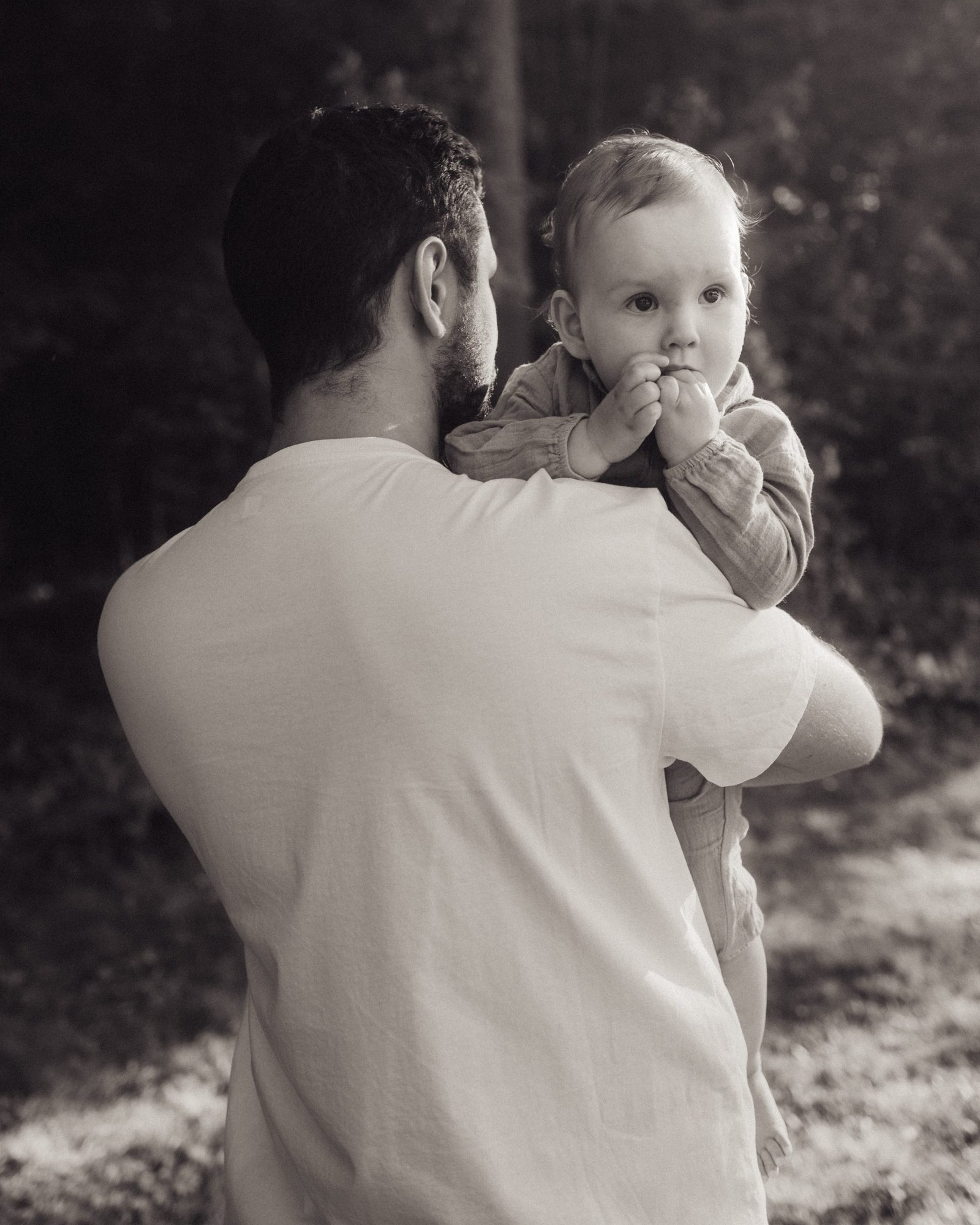 A father holding his son against his chest with sunlight coming through the trees behind them