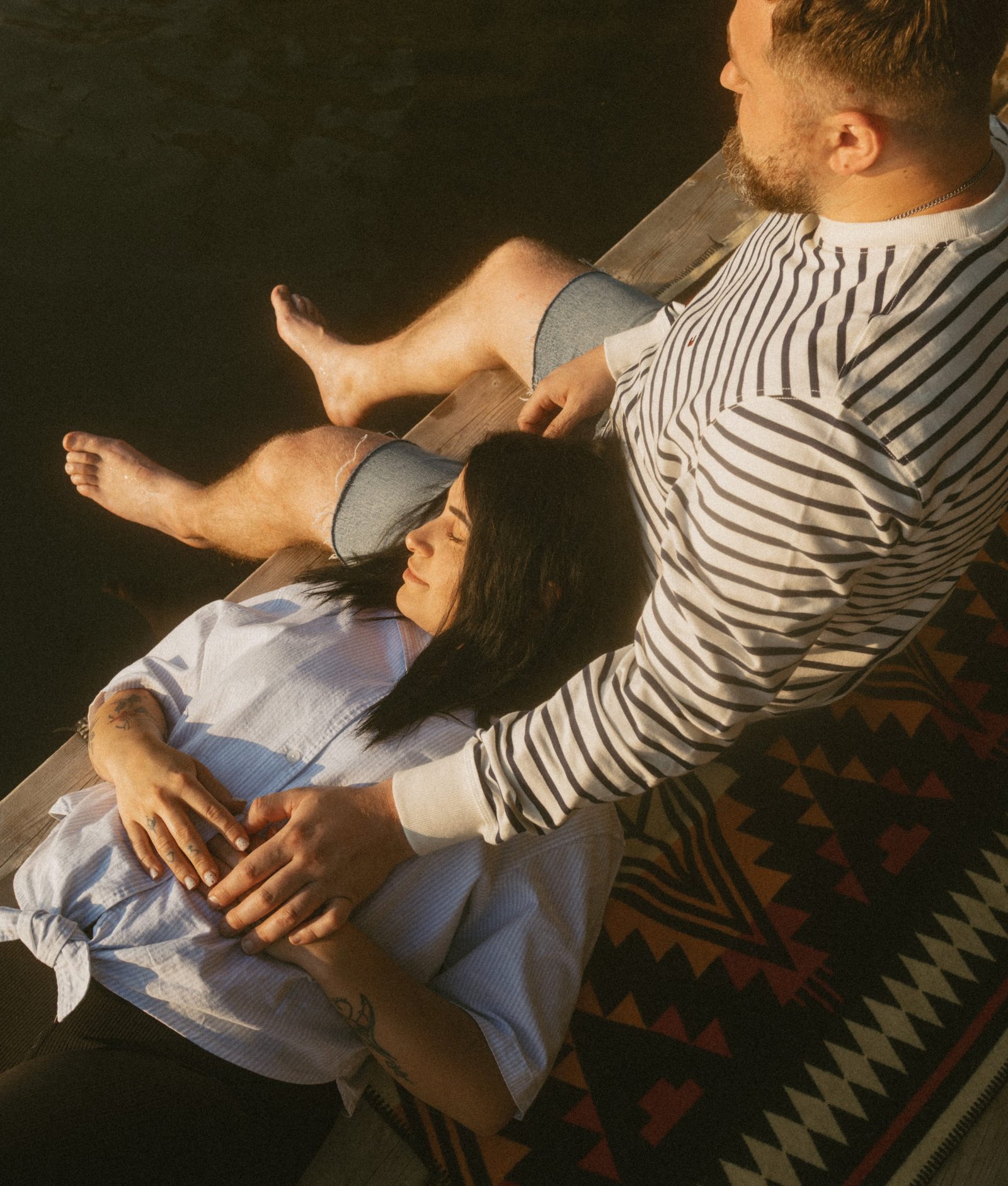 A couple sitting on a low swim platform at the edge of the lake in warm evening light