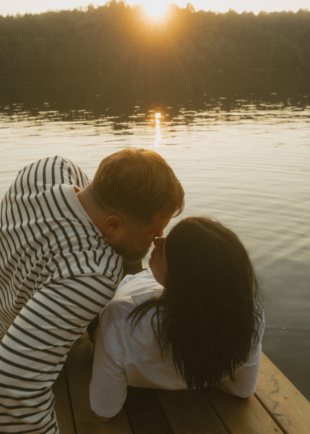 A black and white frame of a couple kissing under backlit trees