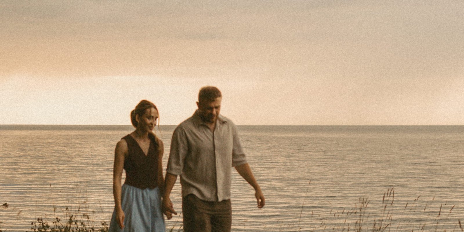 A couple walking along a bluff above Lake Ontario, the sunset glowing through rain clouds over the water behind them