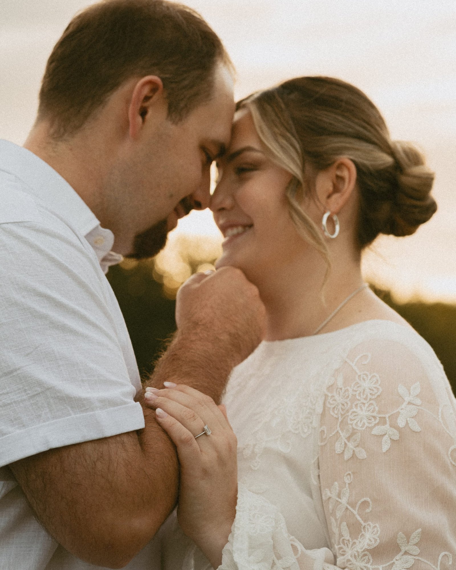A couple standing forehead to forehead in the meadow, her hand resting on his arm