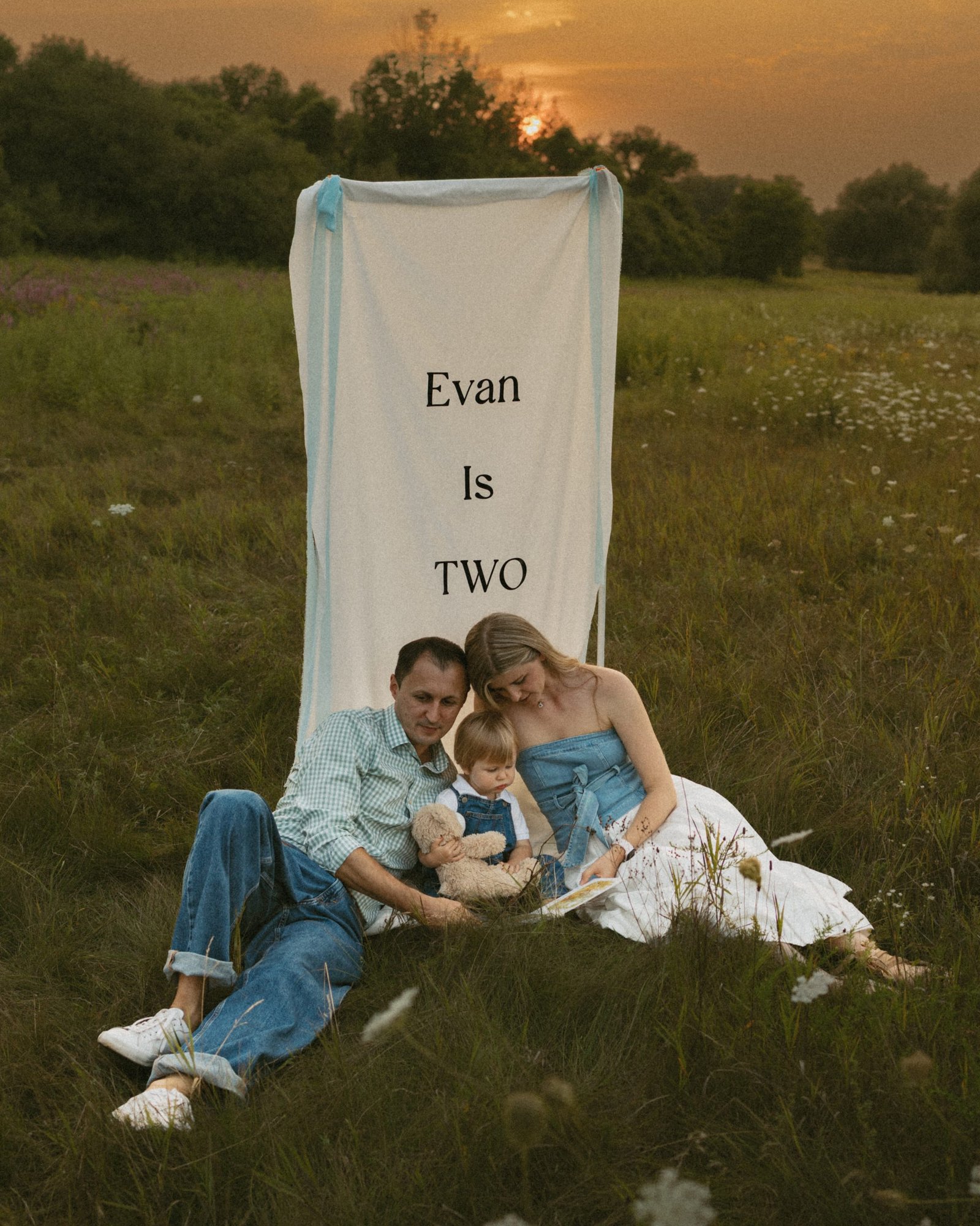 A father, mother and small boy in a meadow with the sun setting behind the treeline