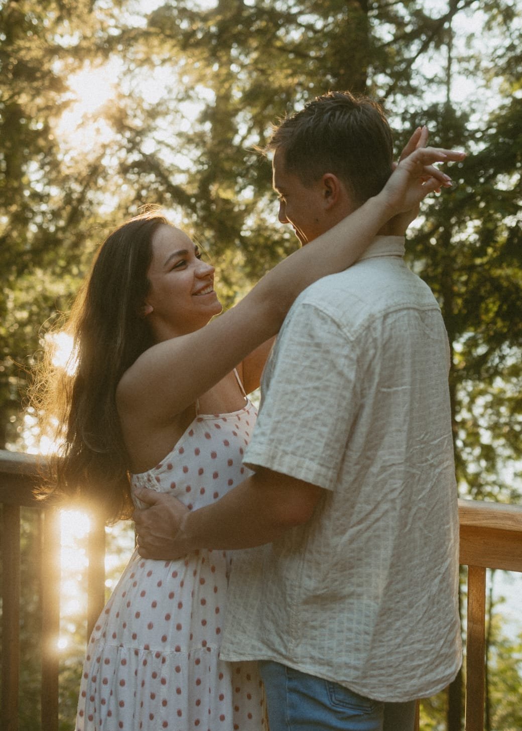 A couple standing forehead to forehead on a cottage deck with sun through the trees