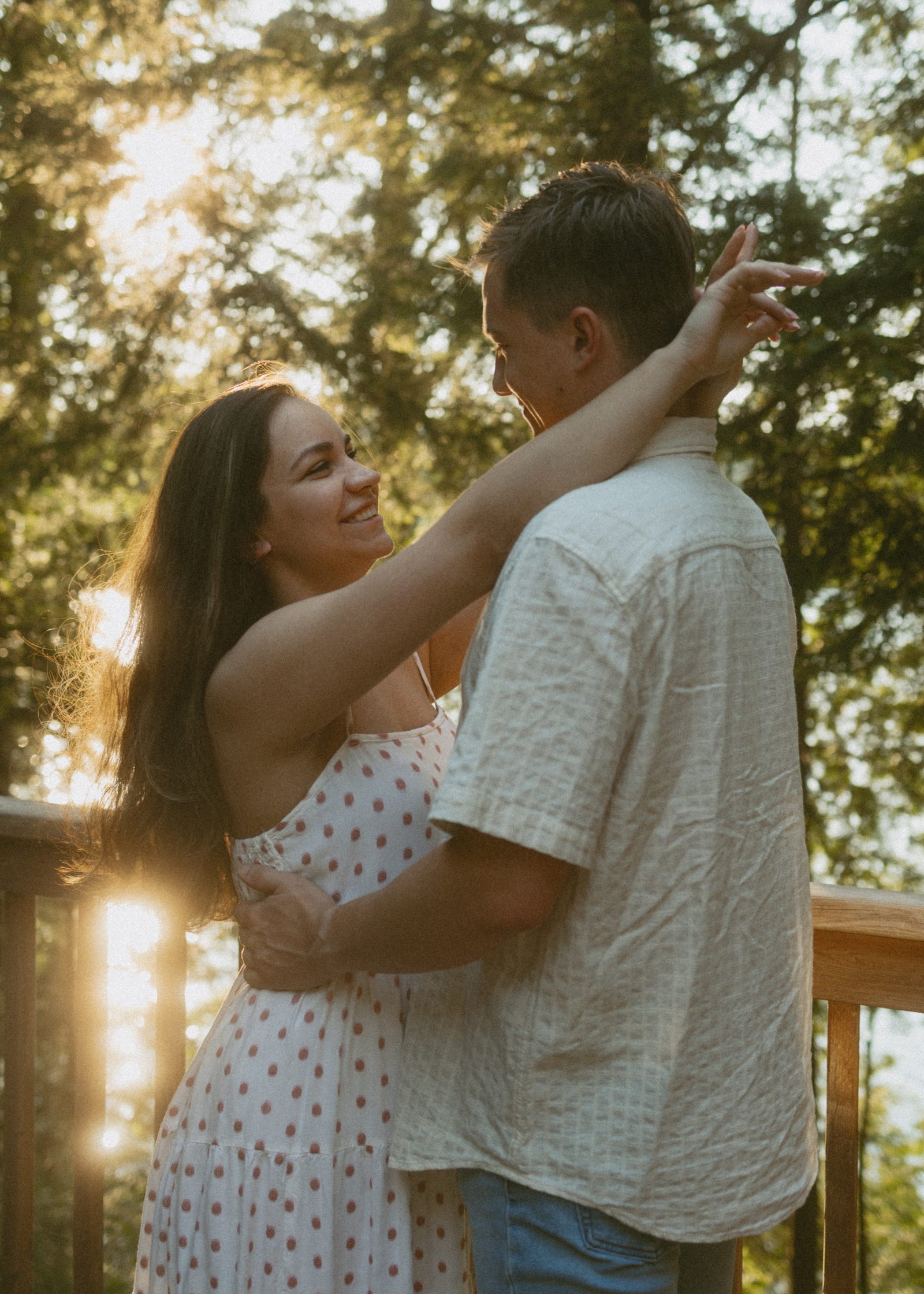 A couple standing forehead to forehead on a cottage deck with sun through the trees