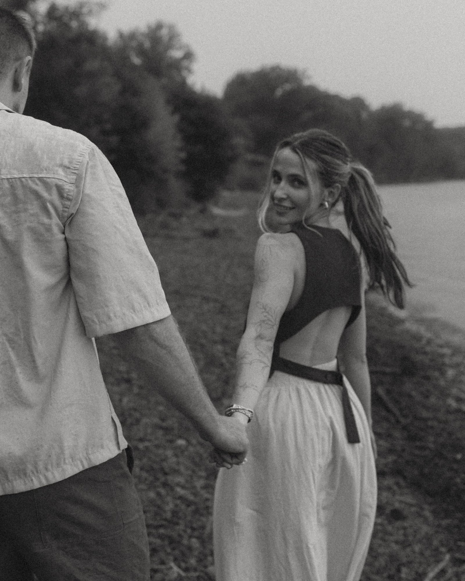 A black and white frame of a woman looking back over her shoulder as she and her partner walk the beach