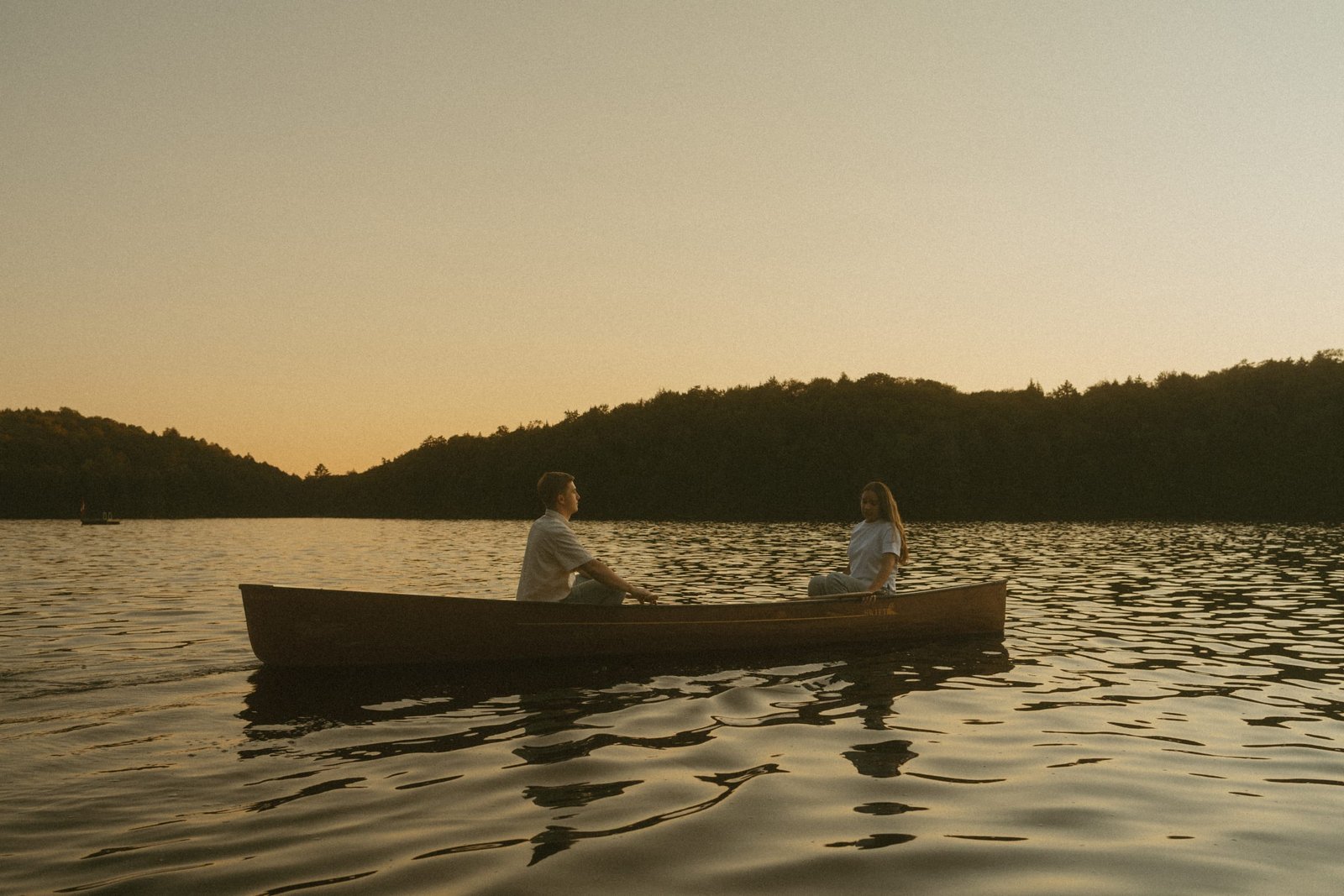 A couple facing each other in a canoe on the water at the end of the day