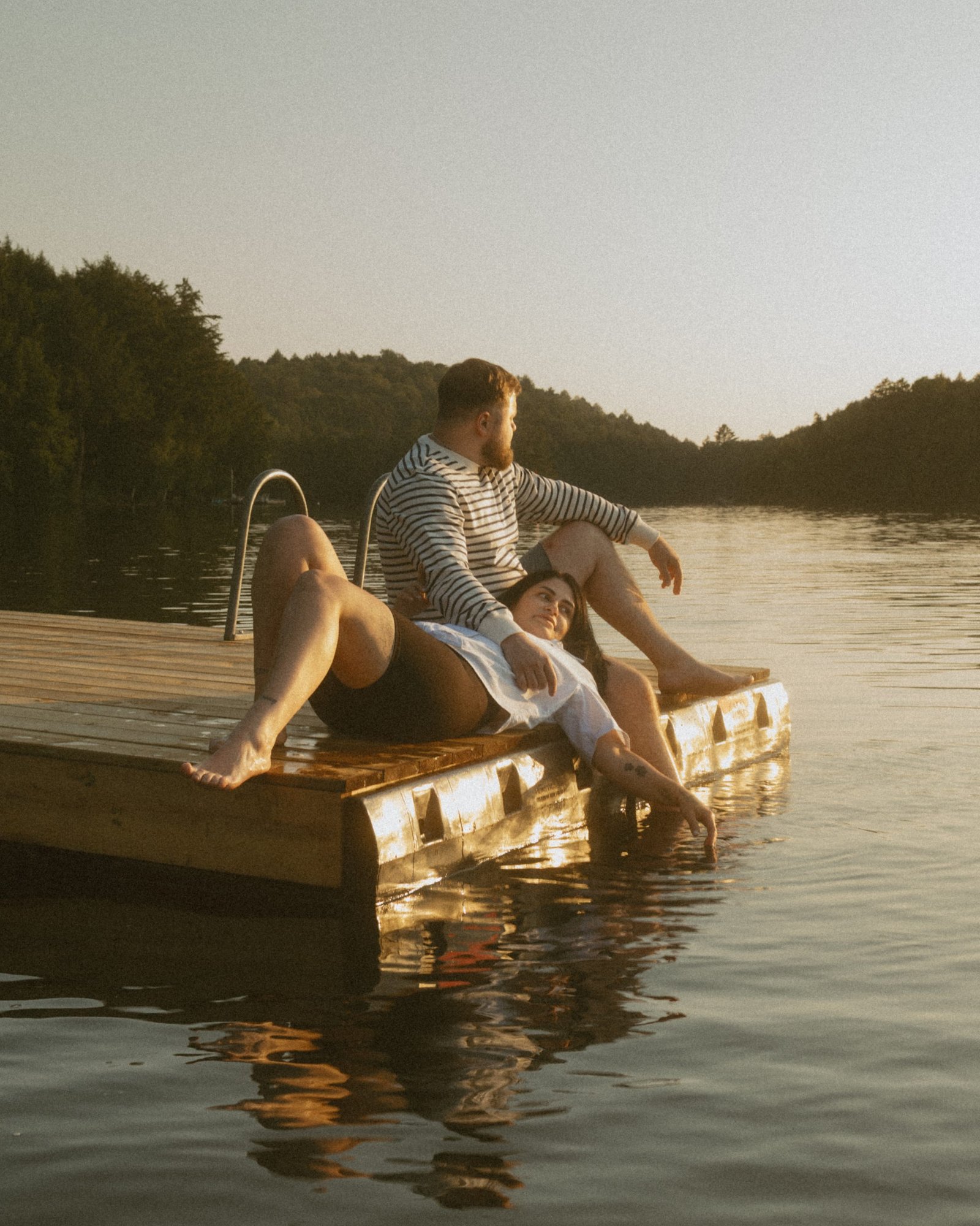 A couple sitting close on the dock, the far shore soft behind them