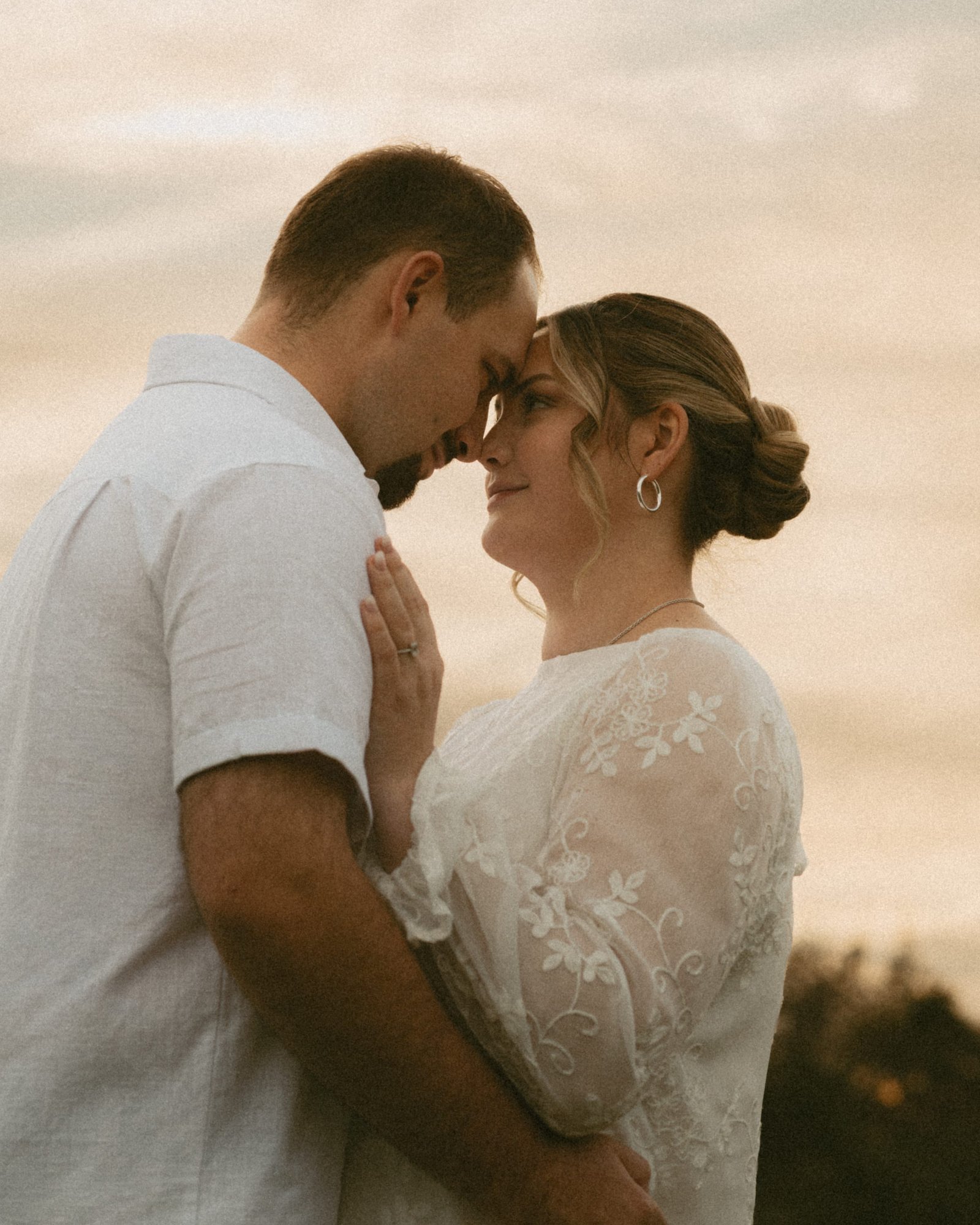 A couple touching foreheads against a pale golden evening sky