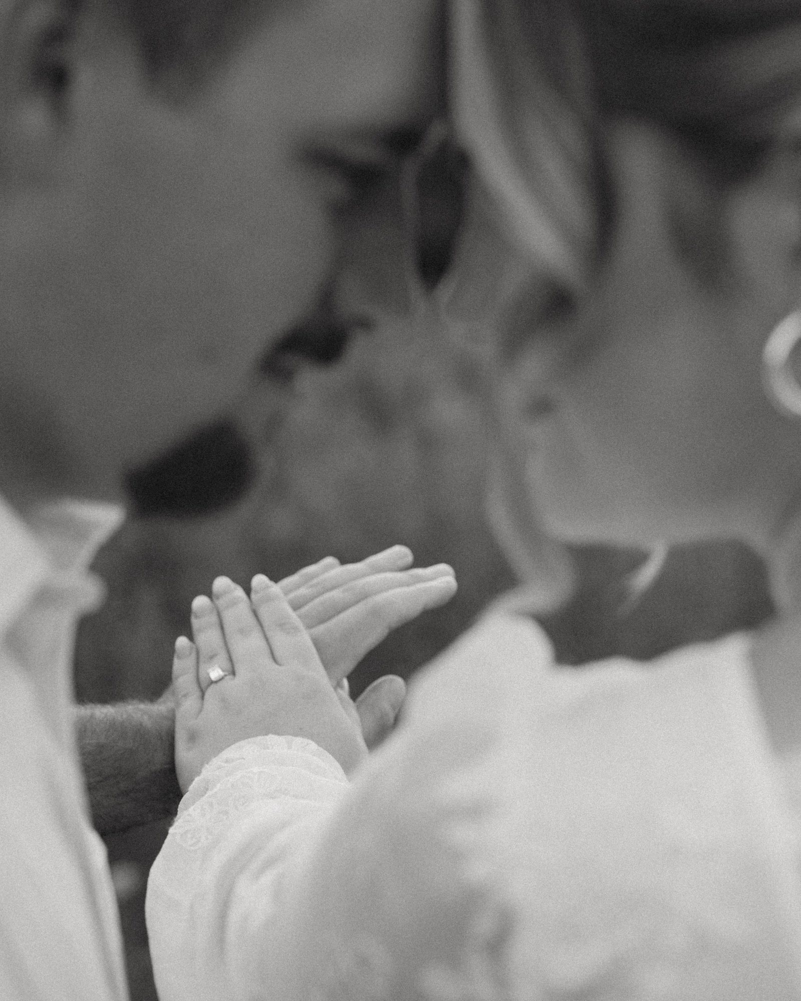 A black and white close-up of a couple nose to nose, her ringed hand raised softly between them