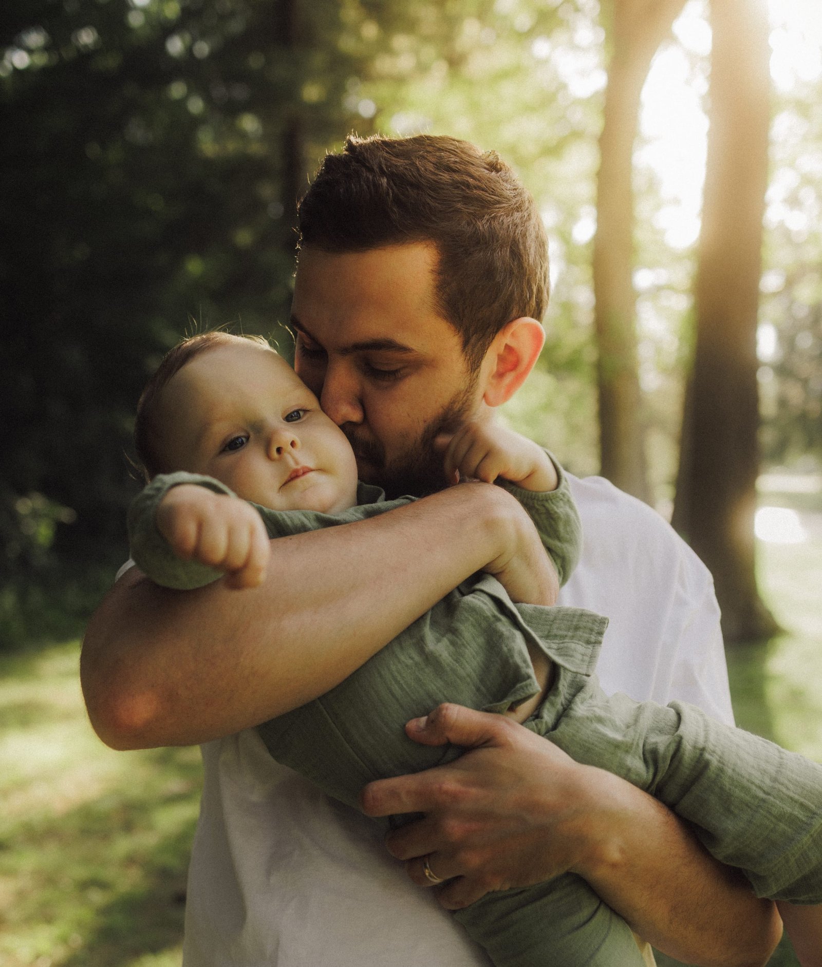 A father carrying his baby son on his shoulder along a backlit woodland path