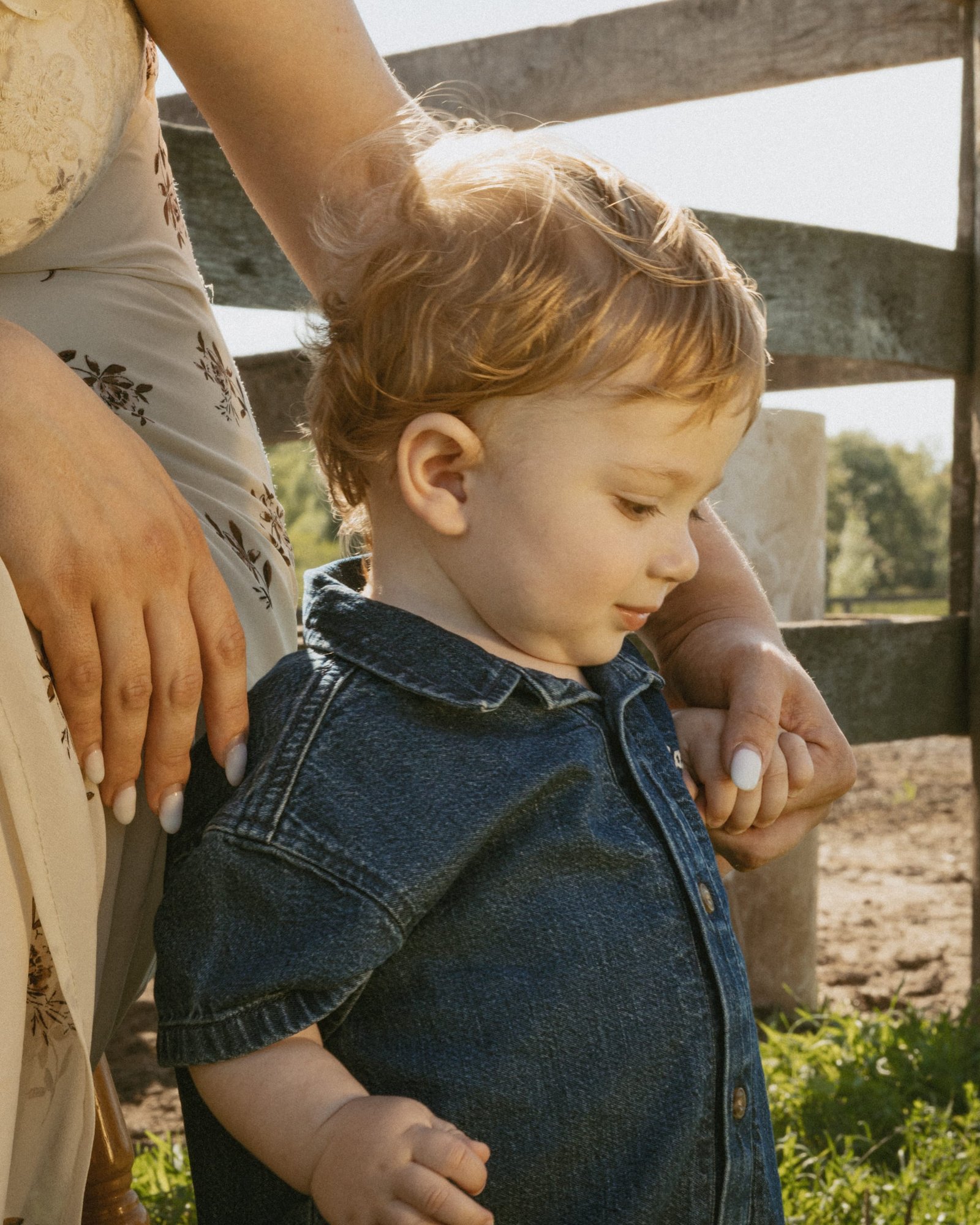 A mother and son sitting together on a chair, both looking off toward the horses