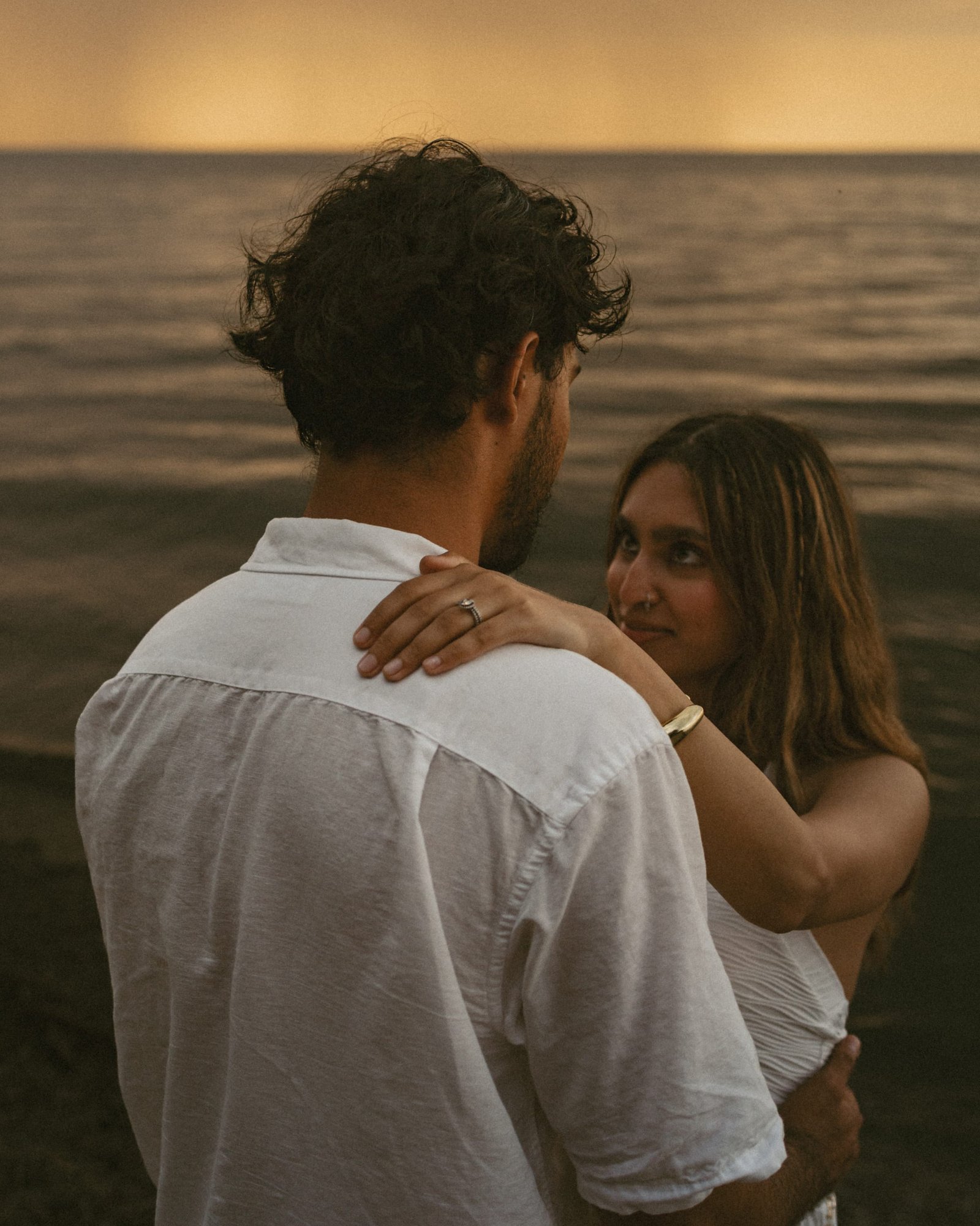 A couple embracing on the shore with the last of the sunlight on the water