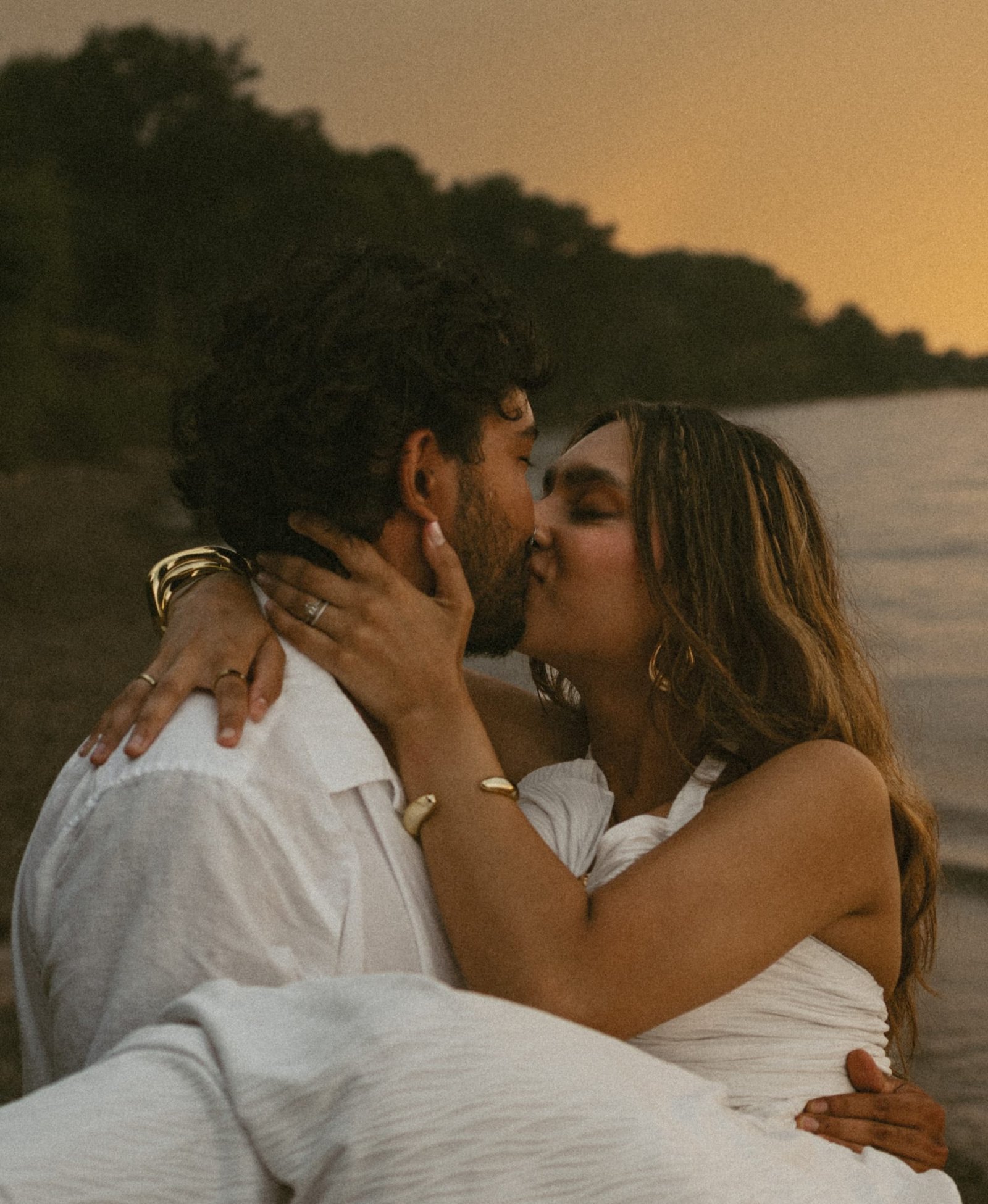 A couple sitting on the shore, her hand on his face and a ring on her finger