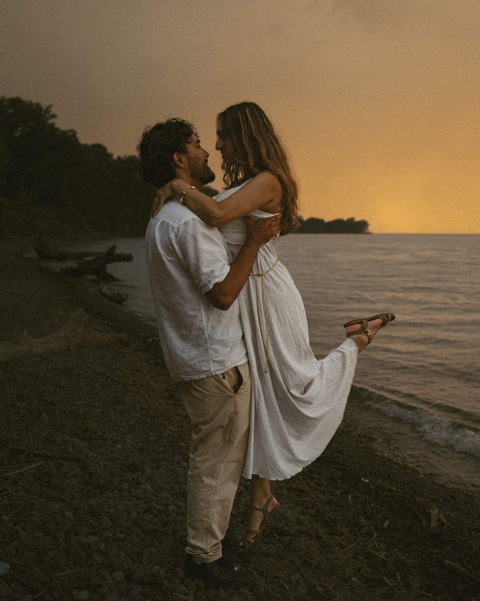A man lifting his partner off her feet on the lakeshore, her dress caught mid-air