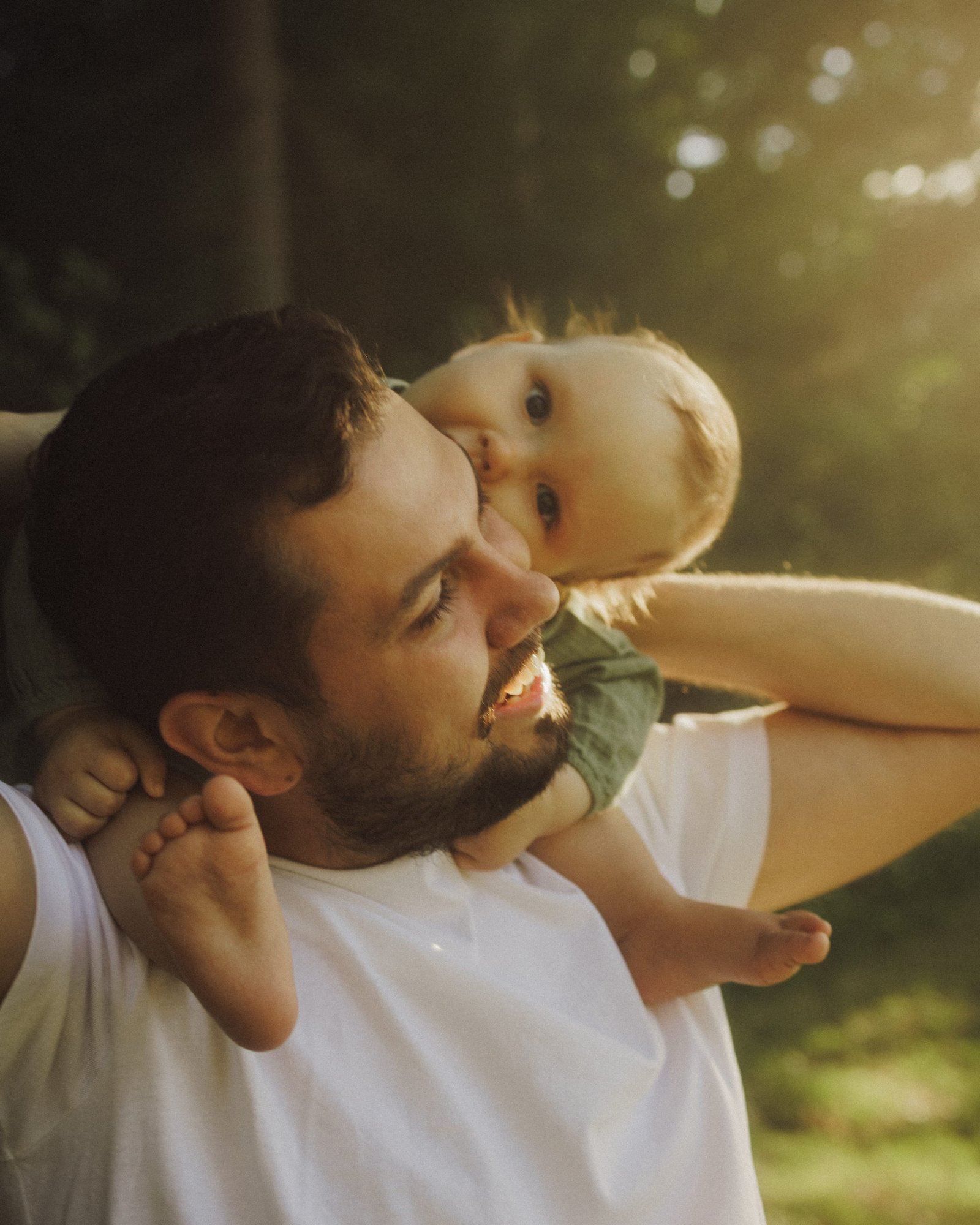 A baby looking back over his father's shoulder on a shaded forest path