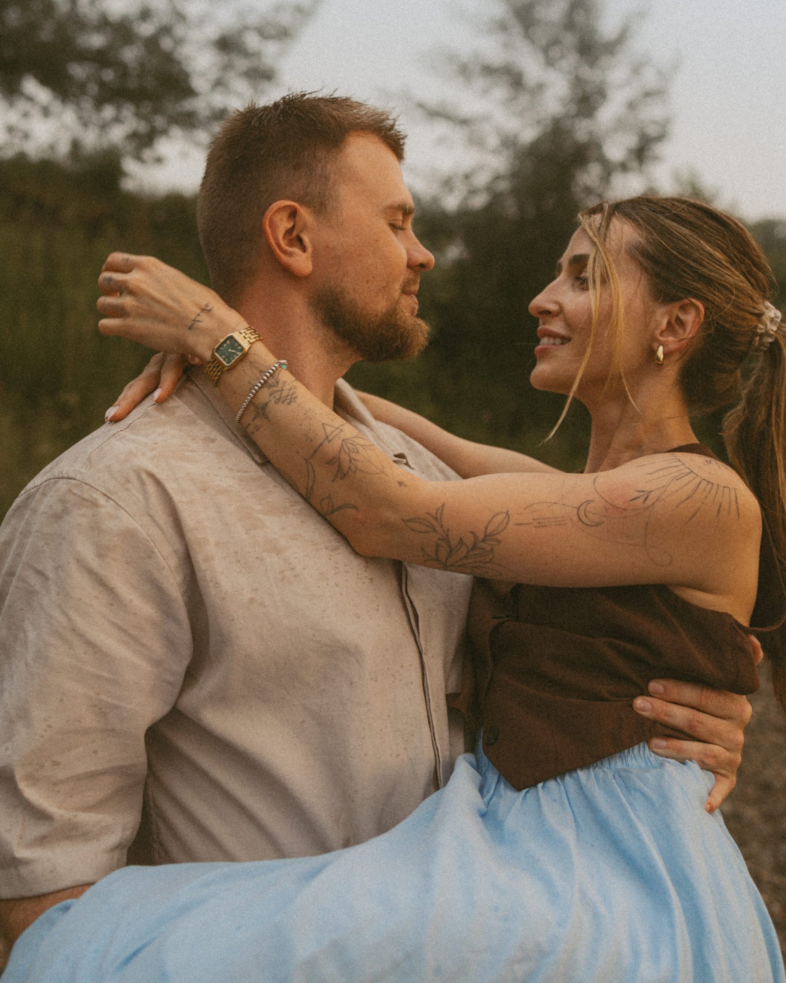 A man holding his partner up in his arms on the beach as she smiles down at him, her arms around his neck