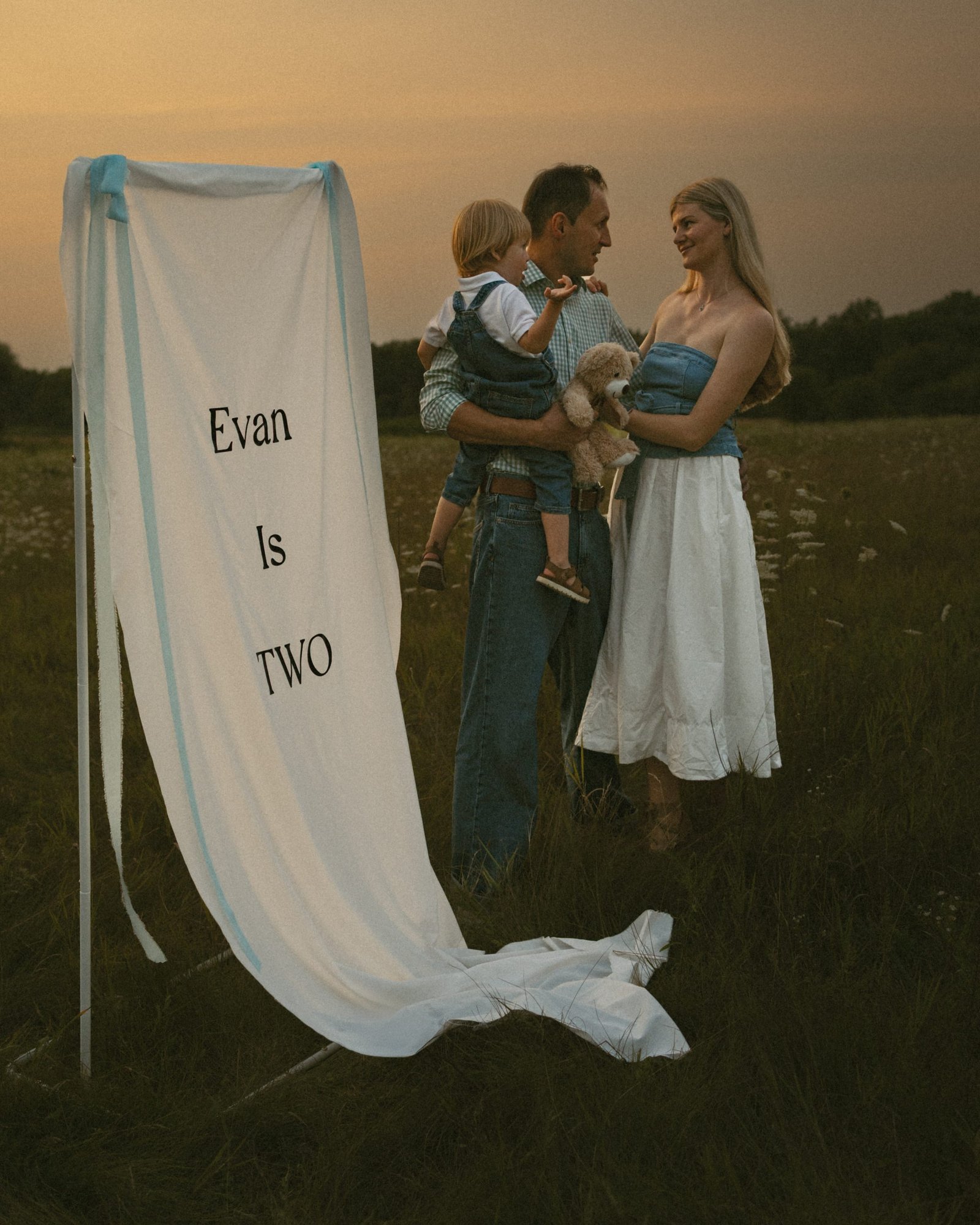 A family standing together in tall grass beside a length of white fabric moving in the wind